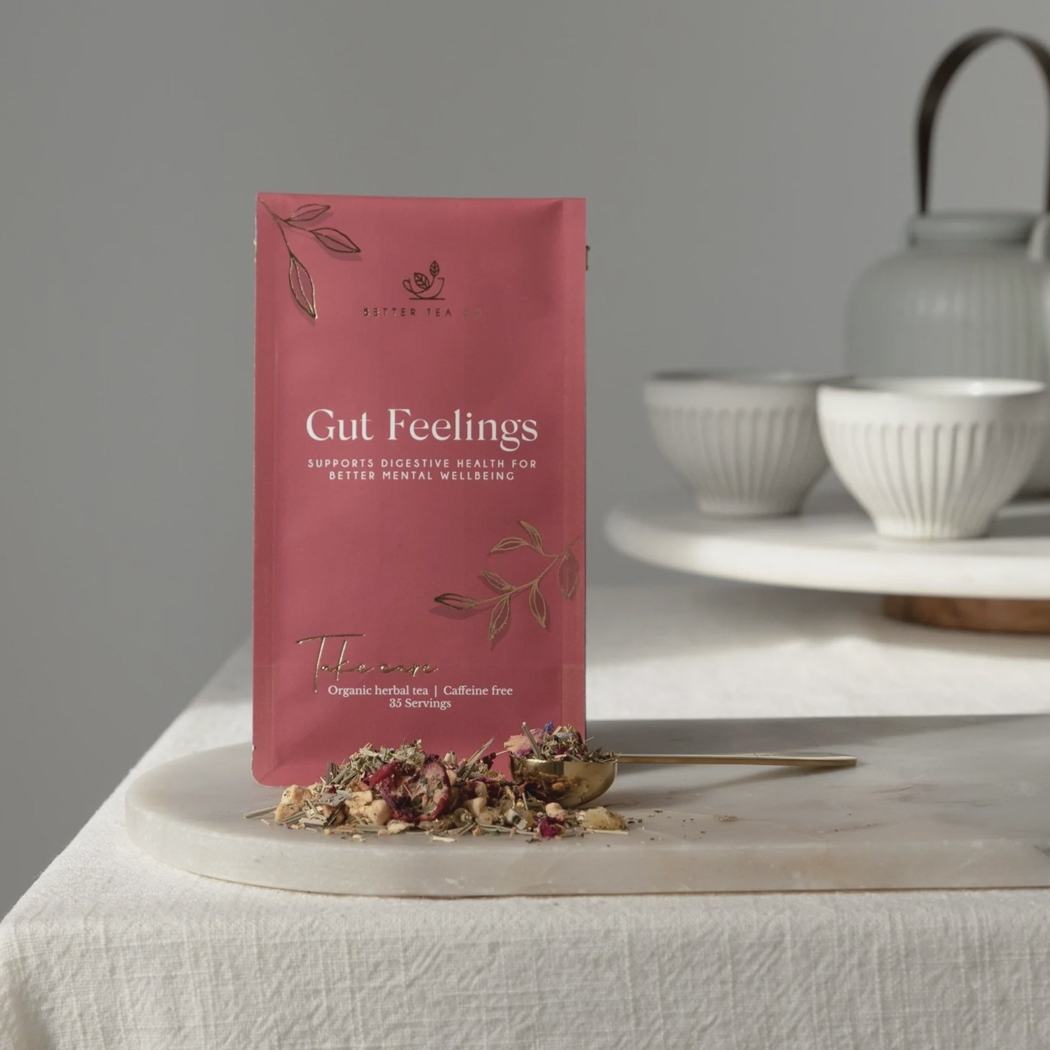 Tea package labeled 'Gut Feelings' on a table with tea leaves and teacups in the background.