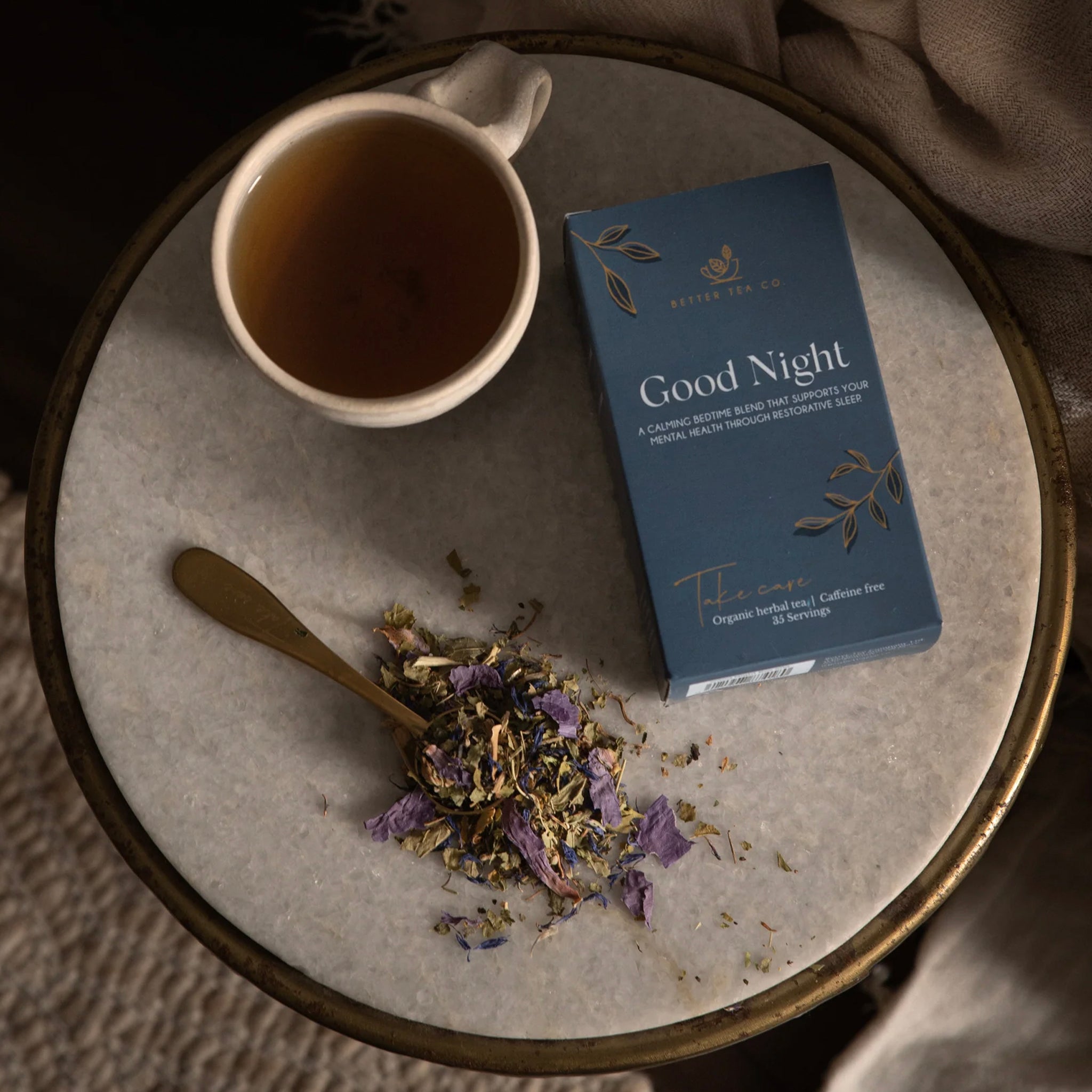 Tea packaging labeled 'Good Night' with a cup of tea and dried tea leaves on a round stone surface.