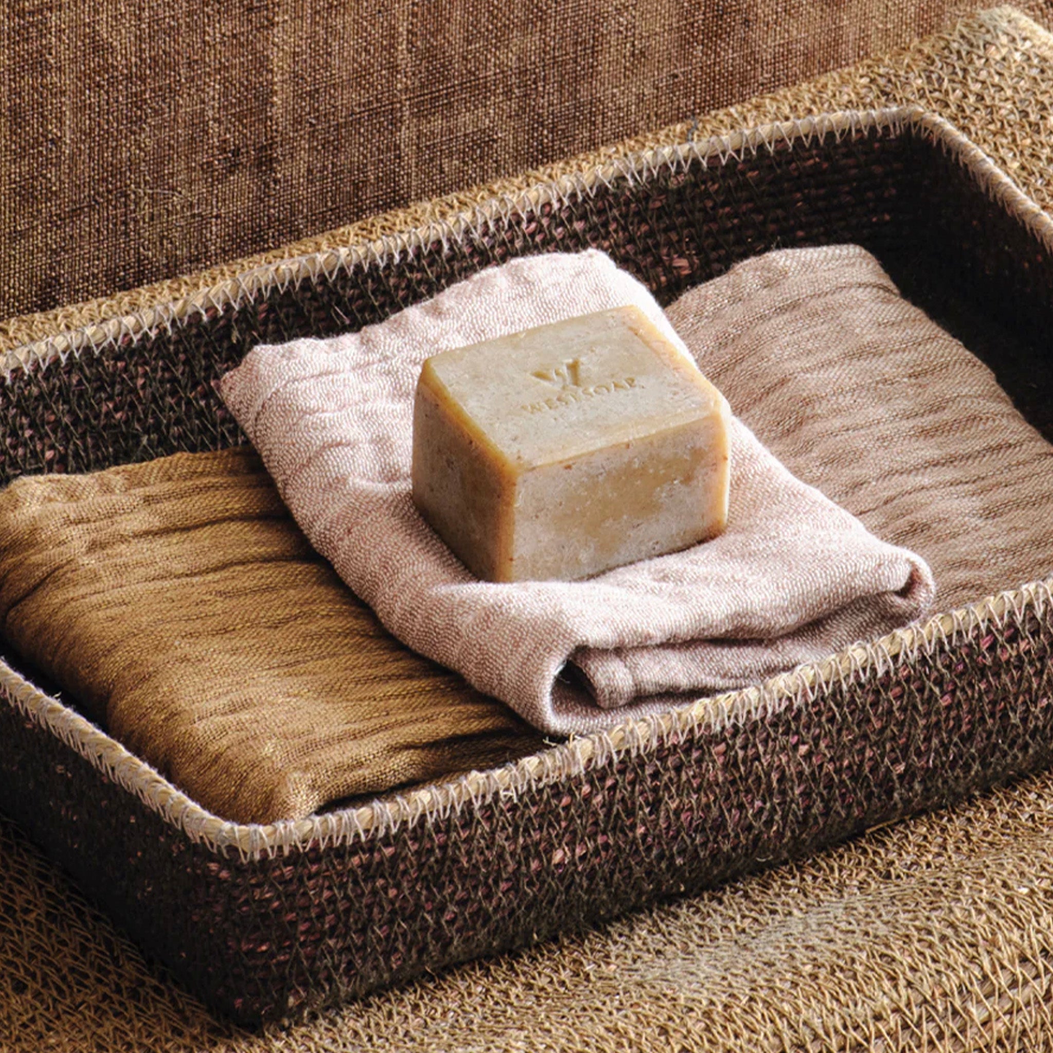 Bar of soap on a folded wash cloth in a woven tray