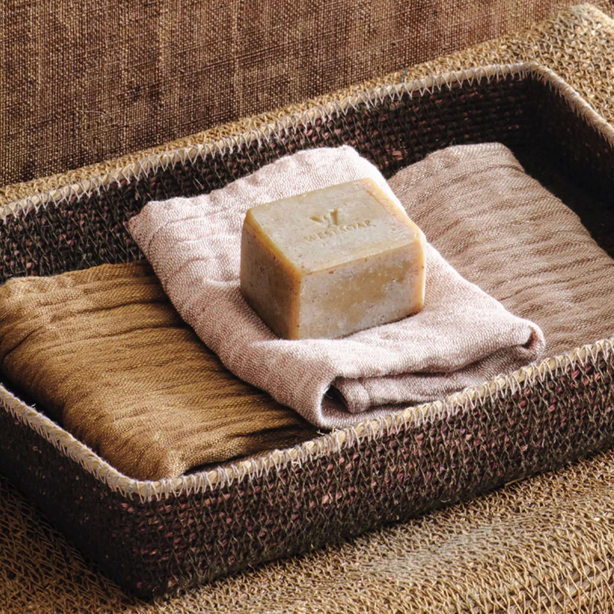 Bar of soap on a folded wash cloth in a woven tray