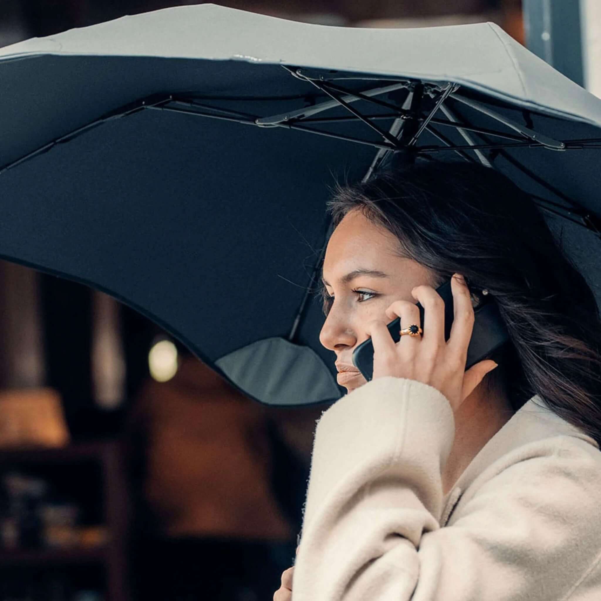 Alt Tag: Blunt Metro Core Range Umbrella in use, compact urban umbrella canopy over commuter on phone in city rain