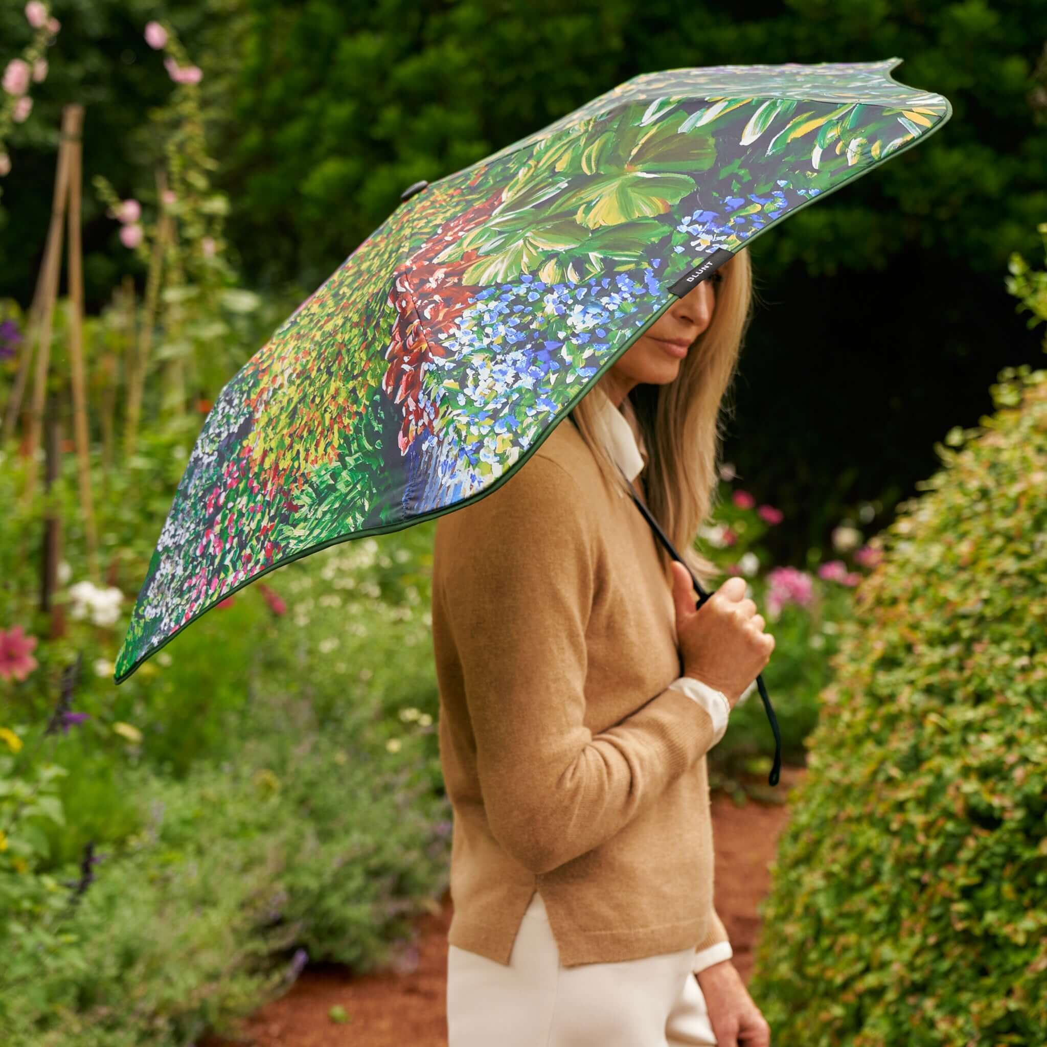 Alt Tag: Blunt Metro Umbrella Karl Maughan 2026 Limited Edition garden art print umbrella held outdoors in lush flower garden