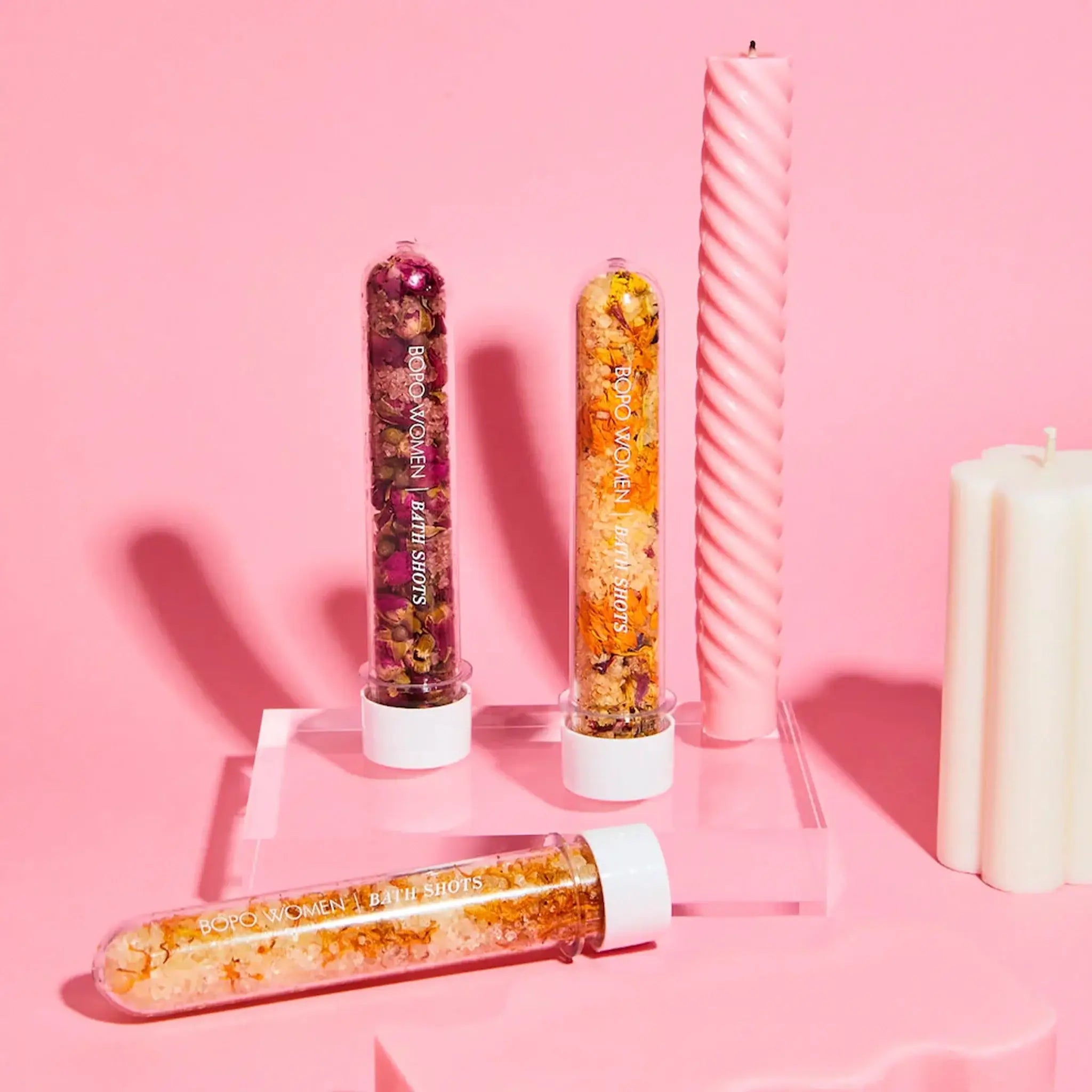 Three decorative vials with colorful contents on a pink background