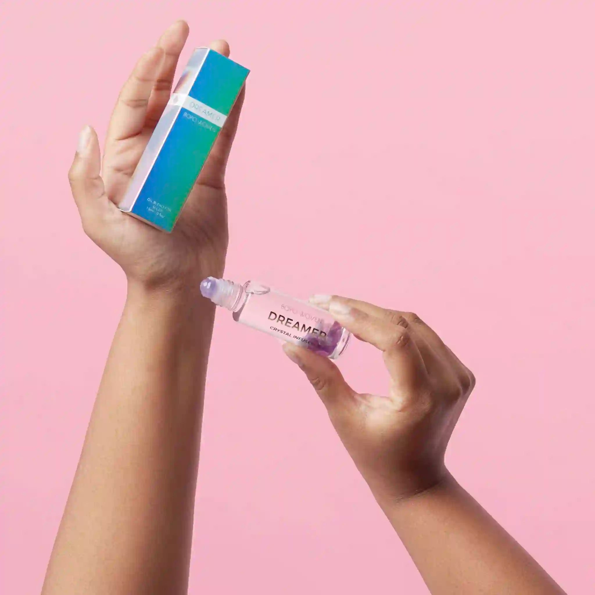 Hand holding a dropper bottle labeled 'Dreamer' with a box on a pink background