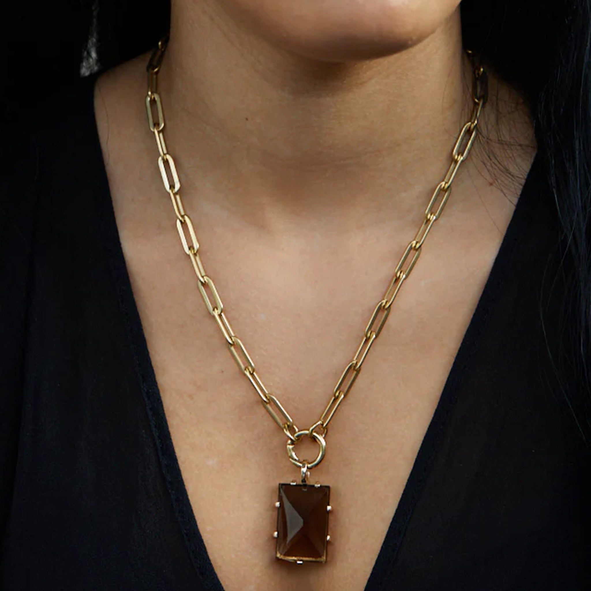 Gold chain necklace with a brown pendant worn by a person against a black background