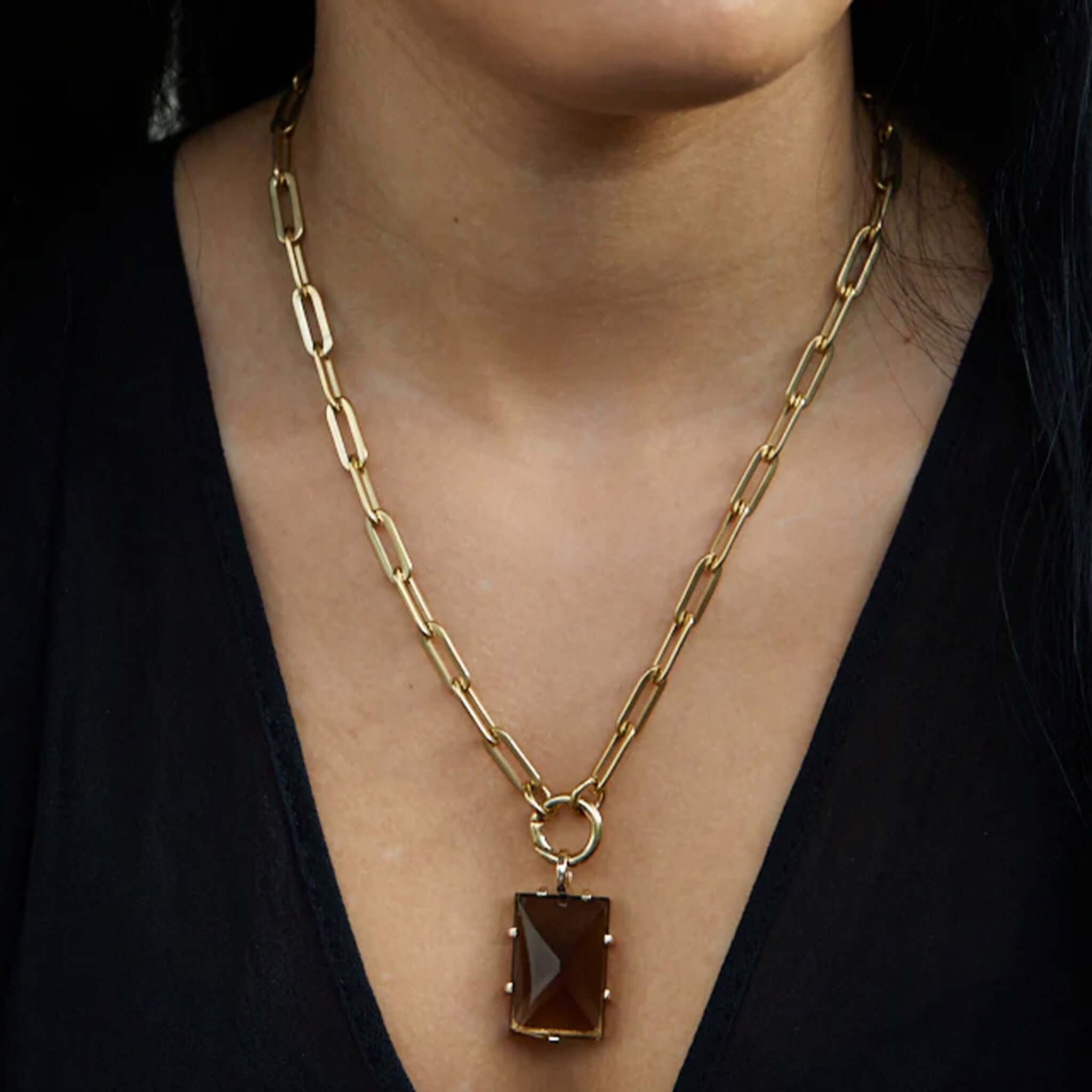 Gold chain necklace with a brown pendant worn by a person against a black background
