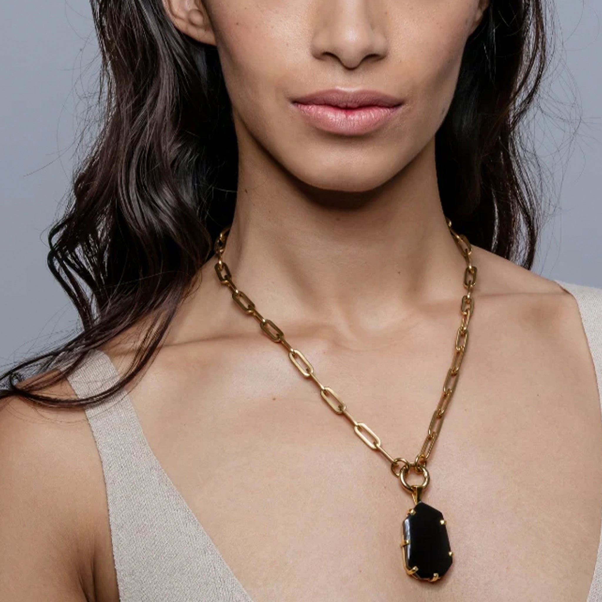 Woman wearing a gold chain necklace with a black pendant against a neutral background