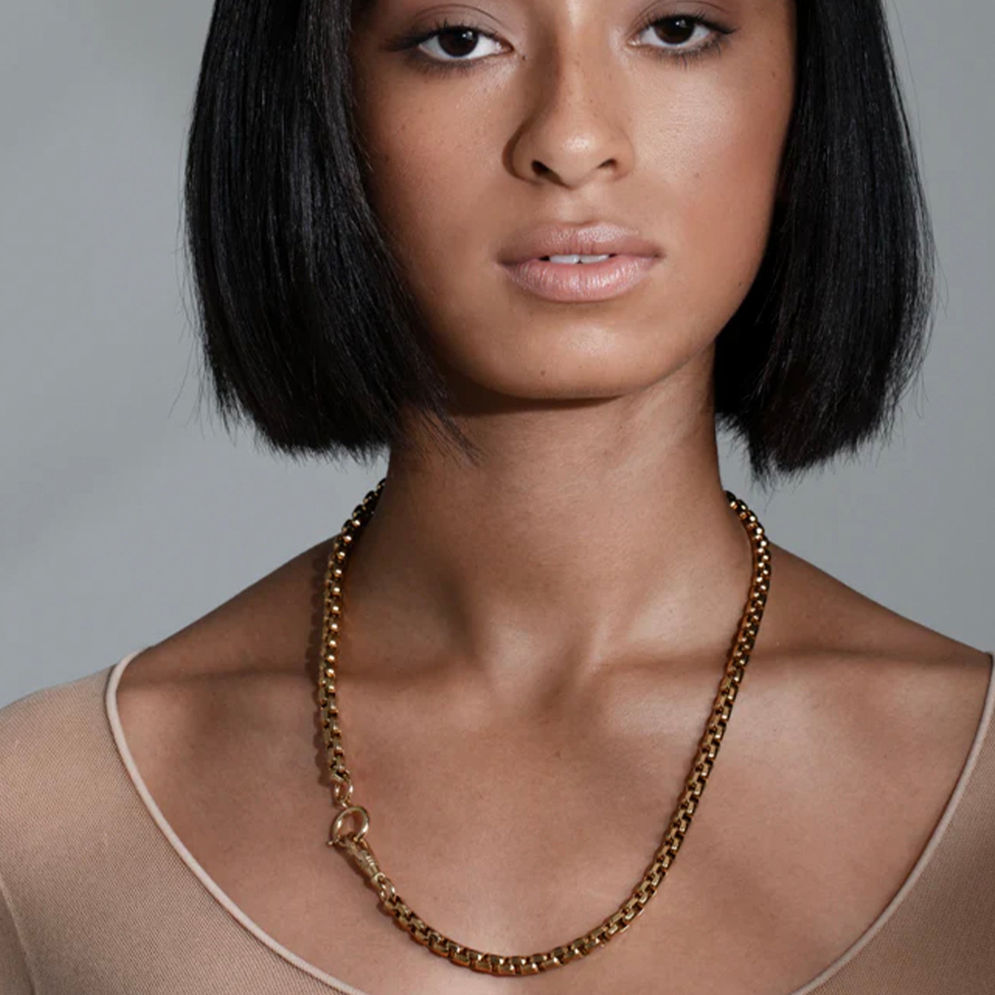 Woman wearing a gold chain necklace on a grey background
