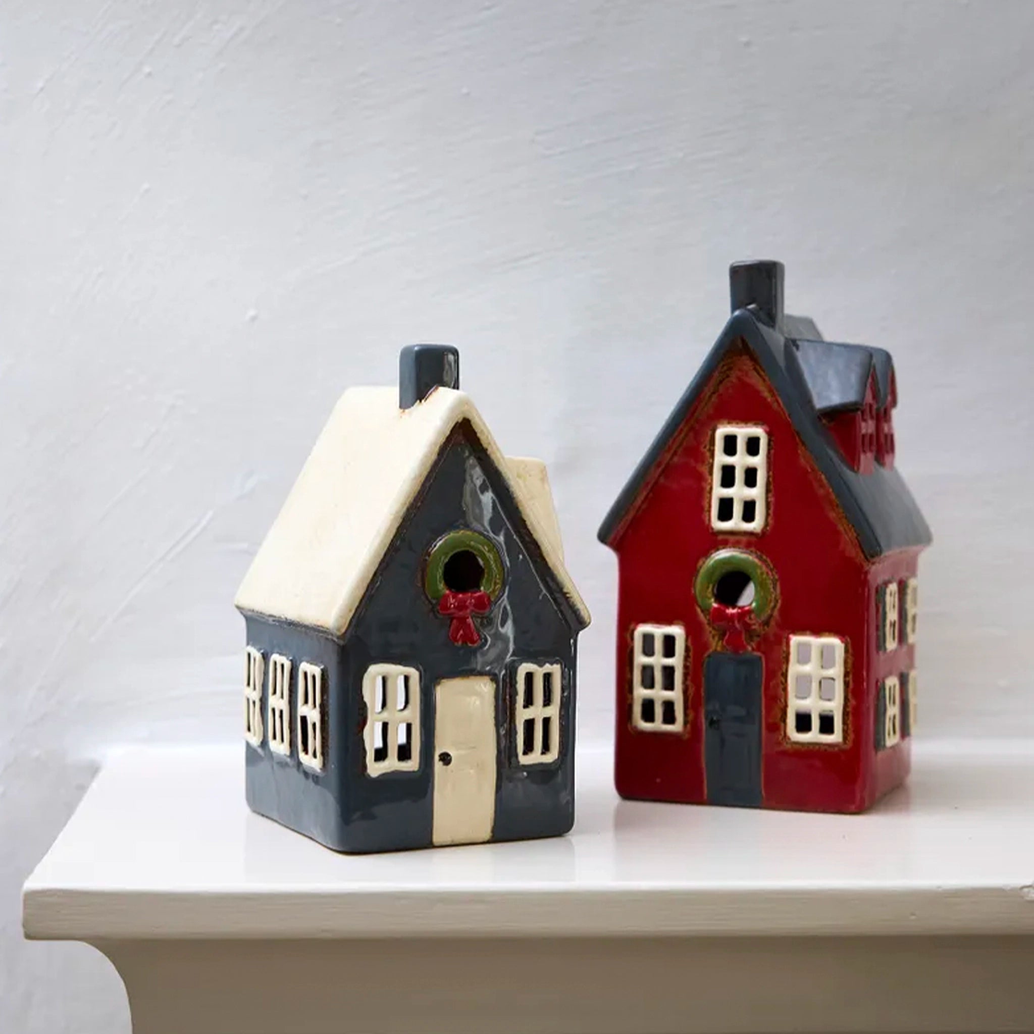 Two ceramic house-shaped vases, one black and white, the other red and black, on a white surface with a light gray background.