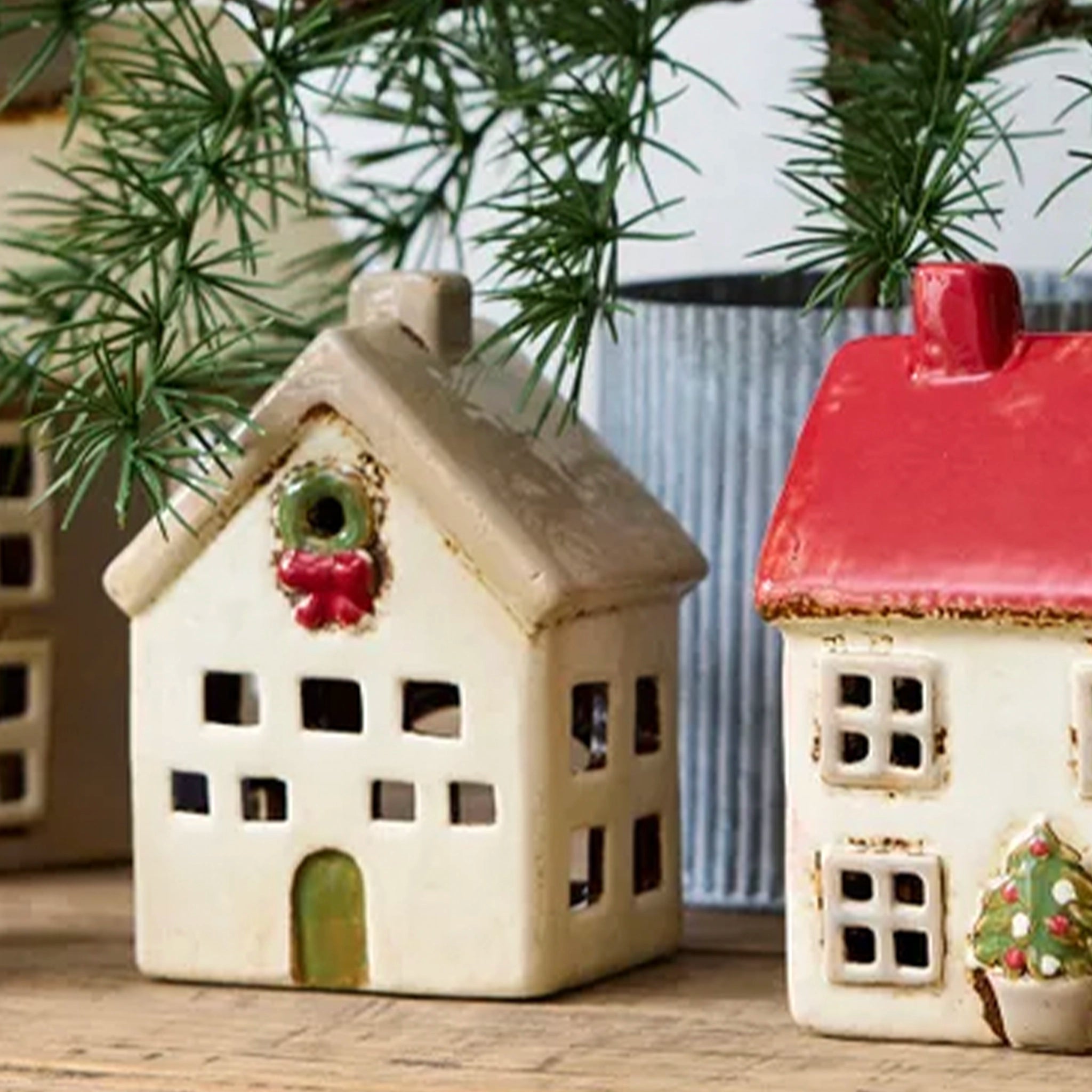 Two small ceramic houses with decorative elements on a wooden surface with greenery in the background.
