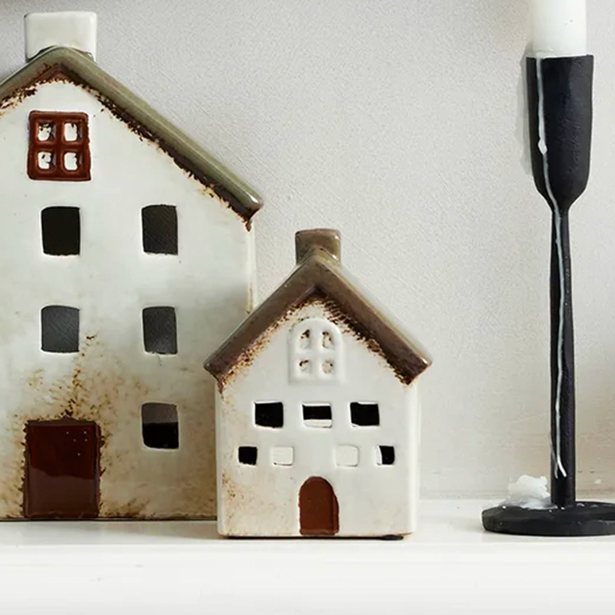 Two ceramic house-shaped lanterns on a white surface with a neutral background