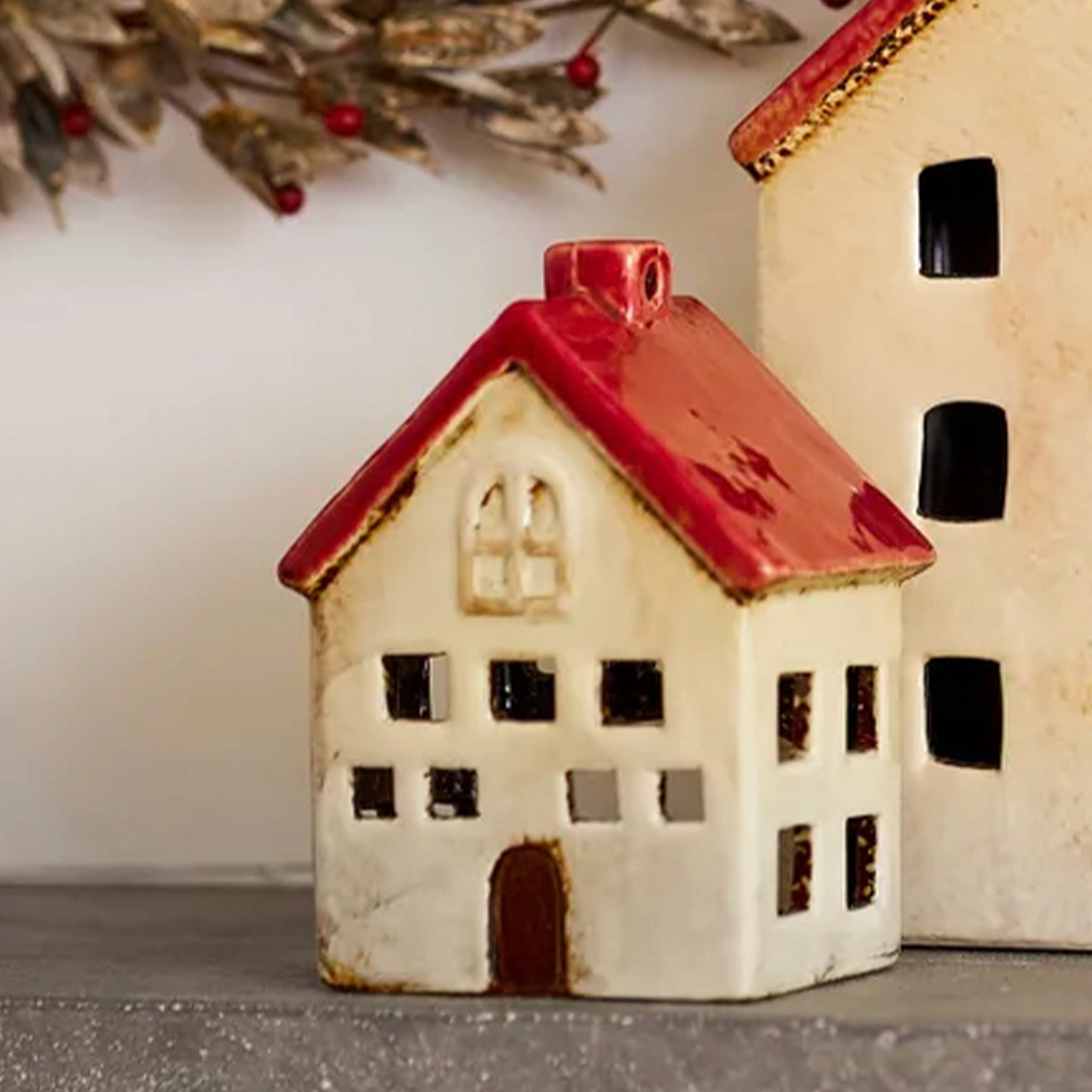 Ceramic house-shaped ornament with red roof and white body on a neutral background