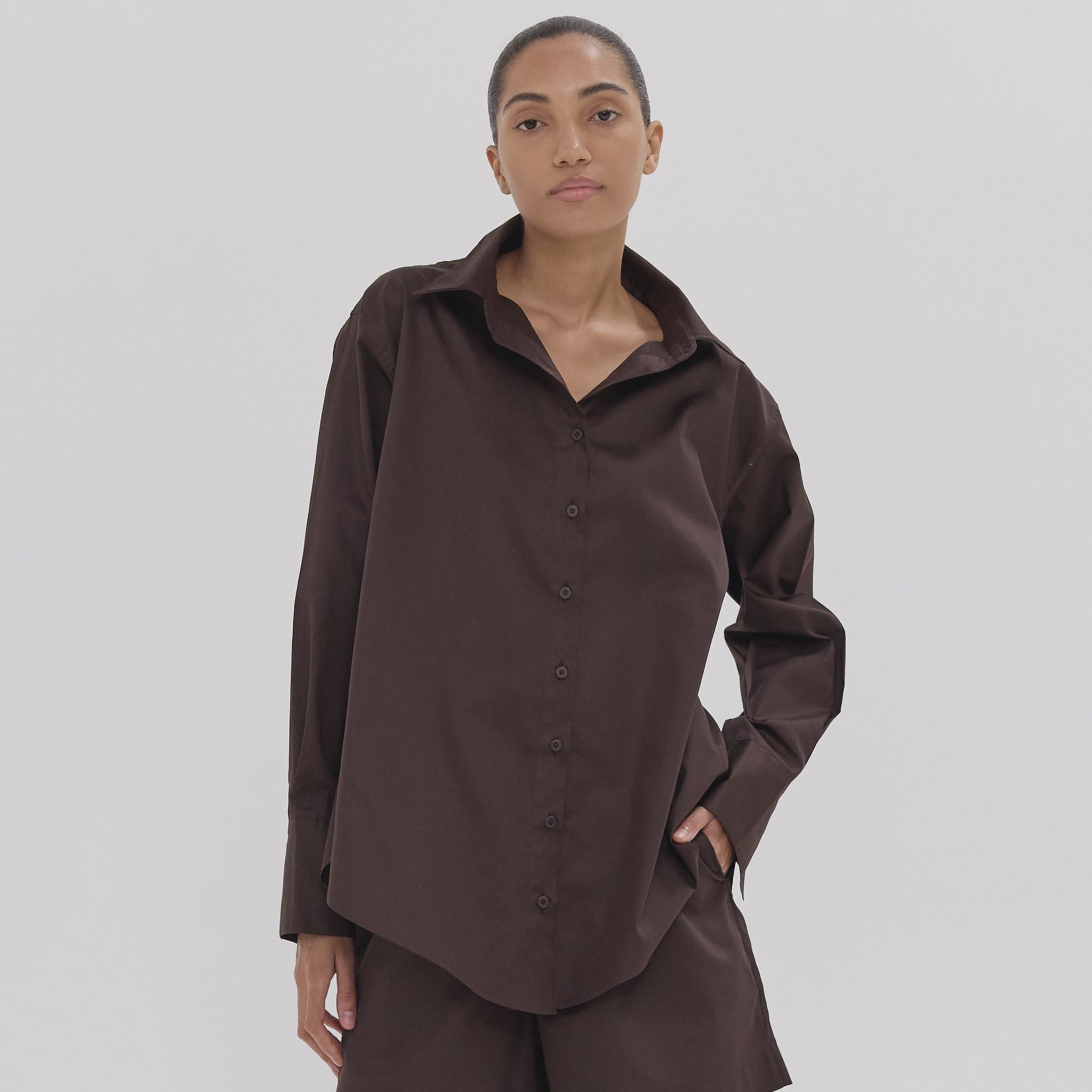 Person wearing a brown button-up shirt and pants on a plain background