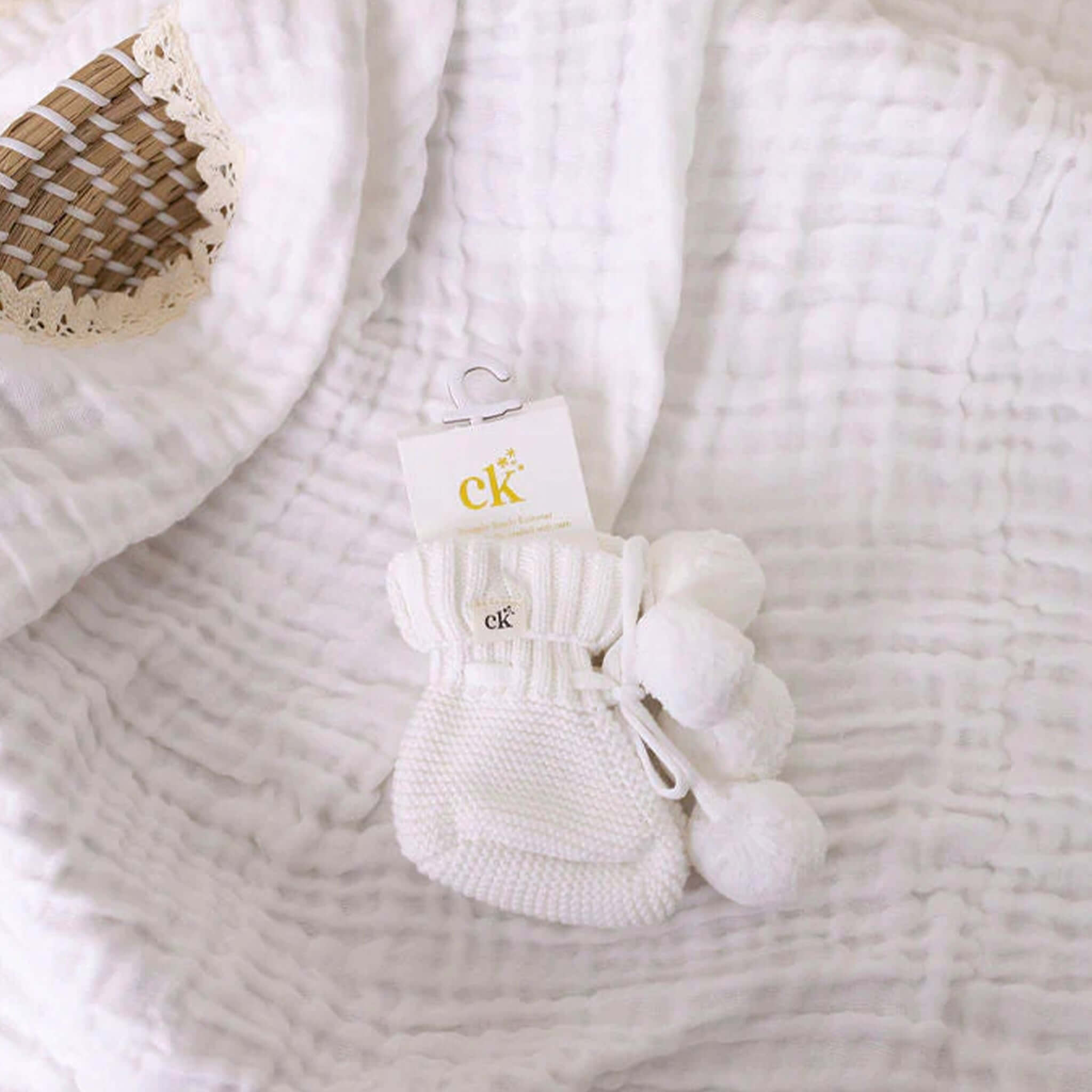 Confetti Kidz Baby Knit Booties - Milk Poms displayed on a soft blanket with pom poms and tag, perfect for tiny feet.