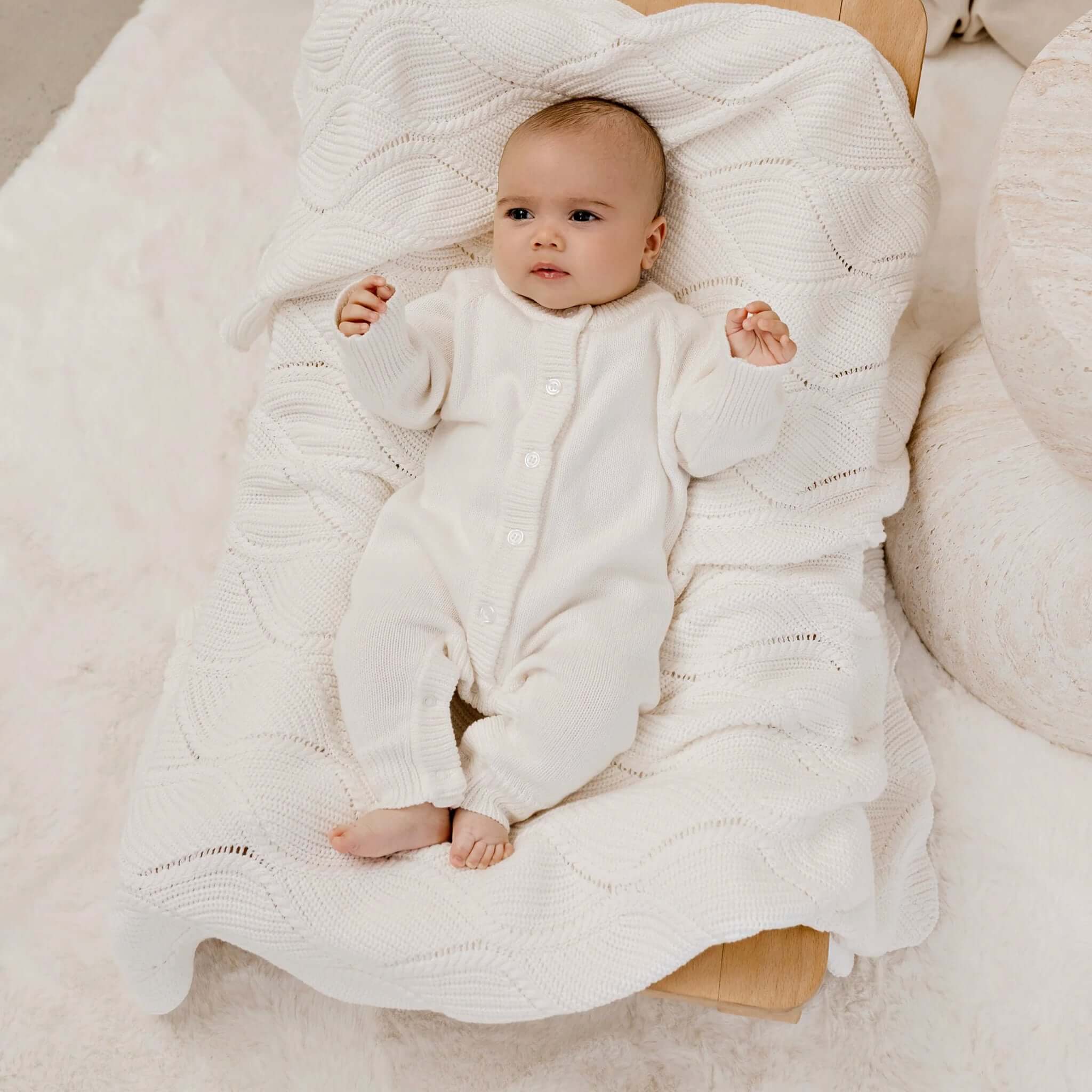 Baby lying on Confetti Kidz Keepsake Knit Blanket - Milk, wrapped in a soft ivory knitted texture.