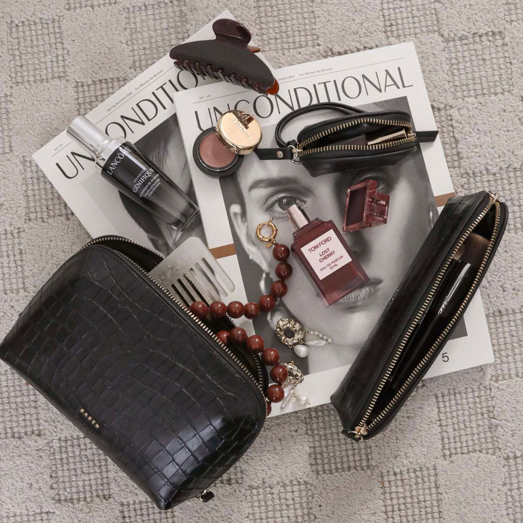 Black handbag with makeup items on a magazine