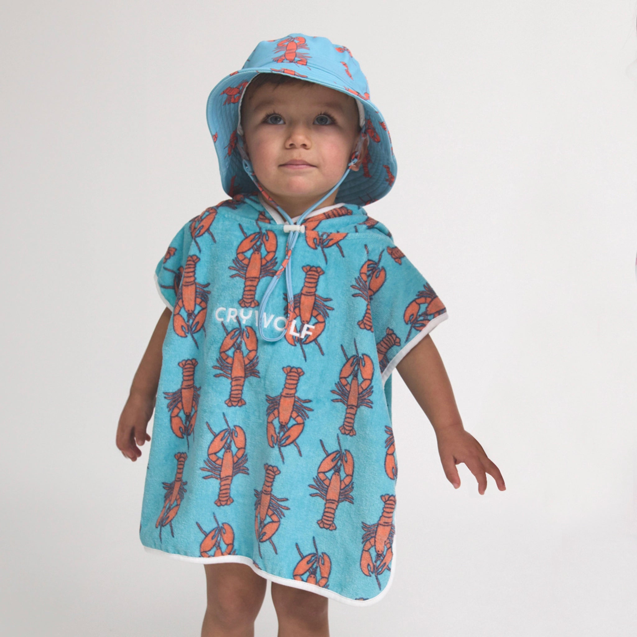 Toddler wearing s hooded poncho with lobster pattern on a light background