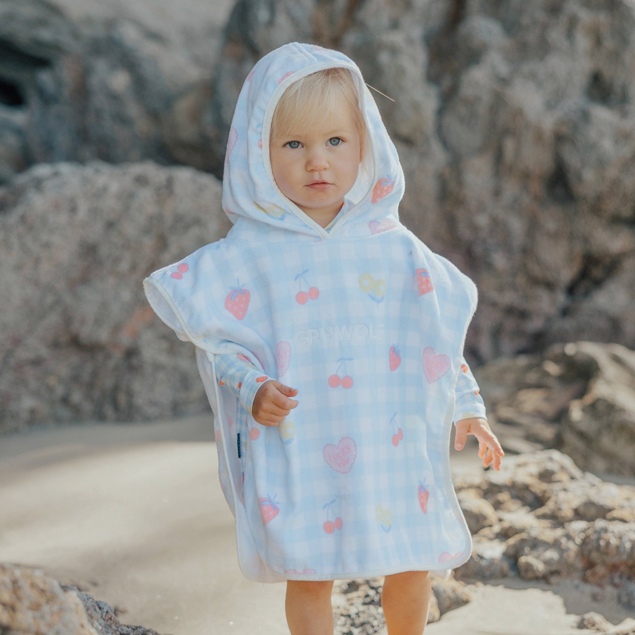 Child wearing a light blue hooded poncho with colorful patterns on a rocky beach.