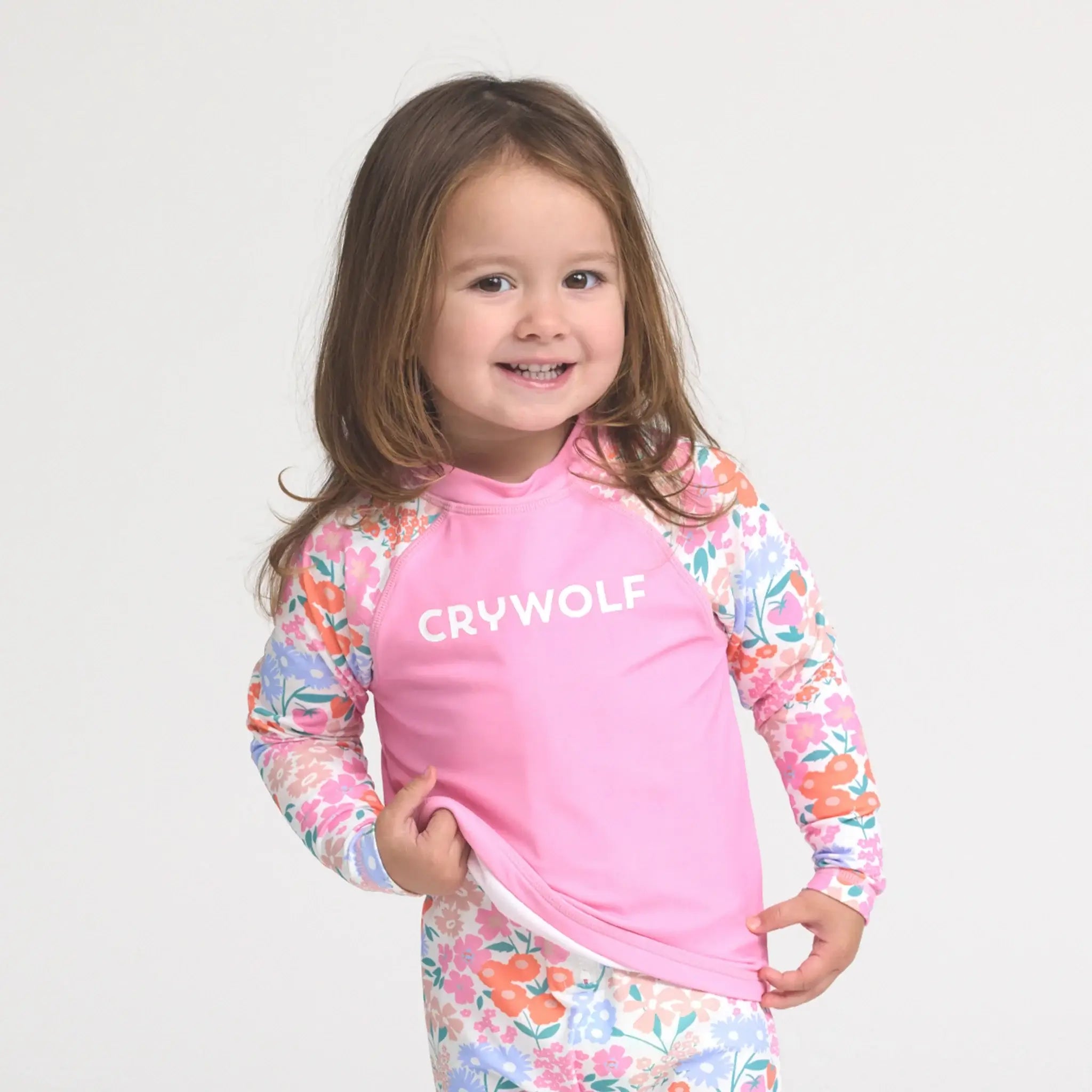 Toddler wearing a pink and floral rash vest on a white background