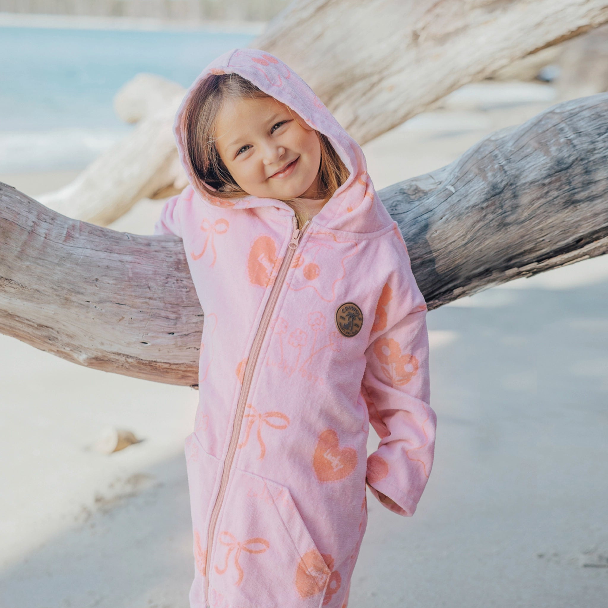 Girl wearing a pink zip up towel with orange floral patterns at a beach