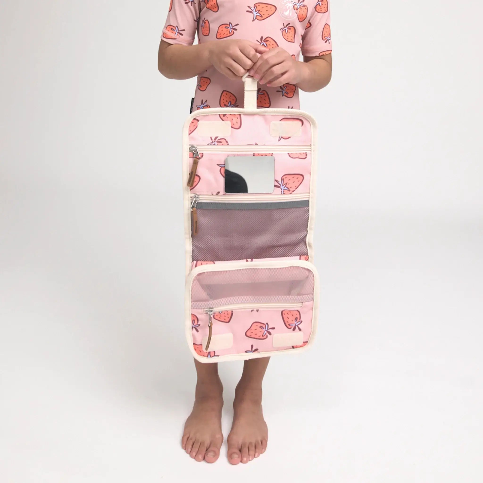 Person holding a pink travel organizer with strawberry pattern on a white background