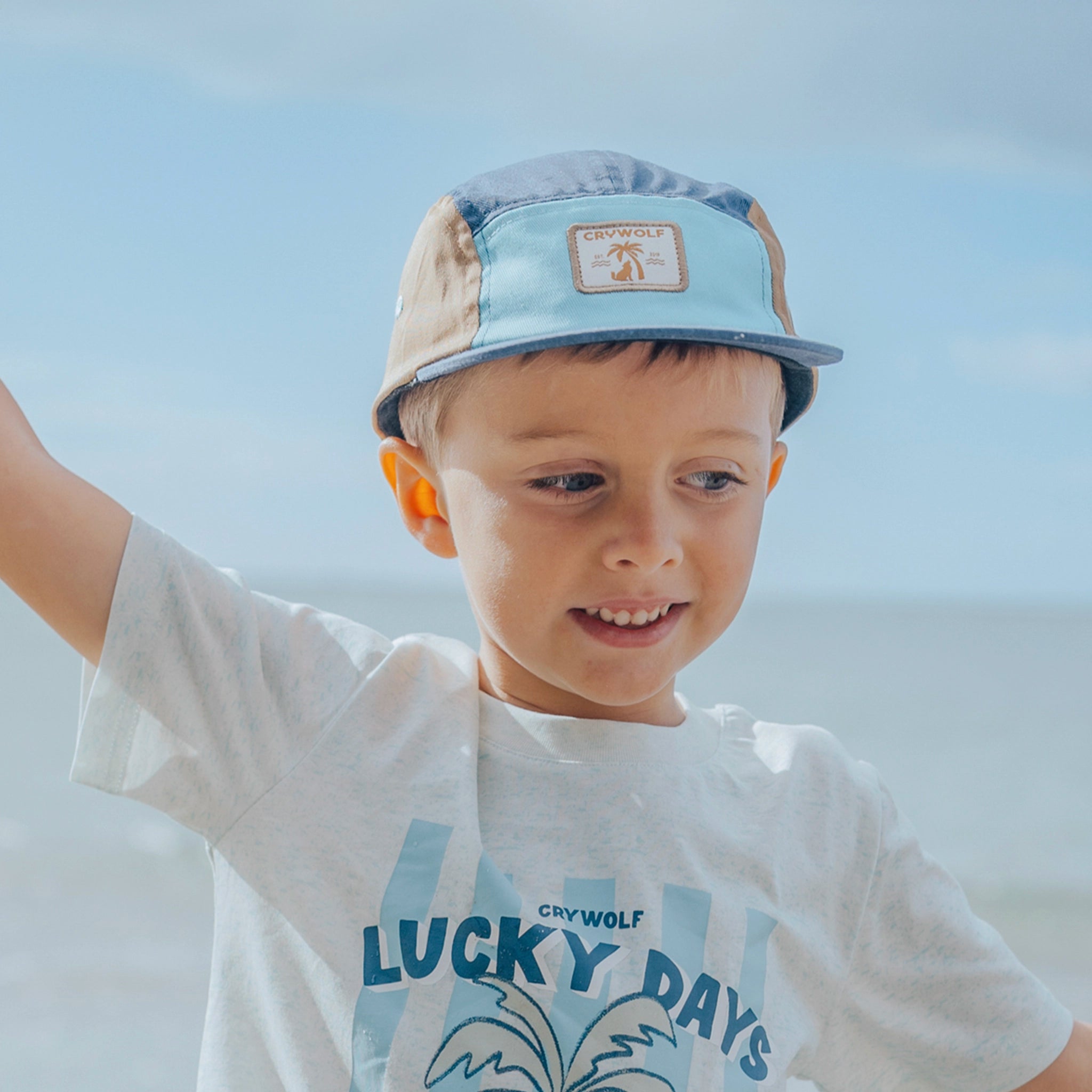 Child wearing a cap and t-shirt with 'Lucky Days' text against a clear sky.