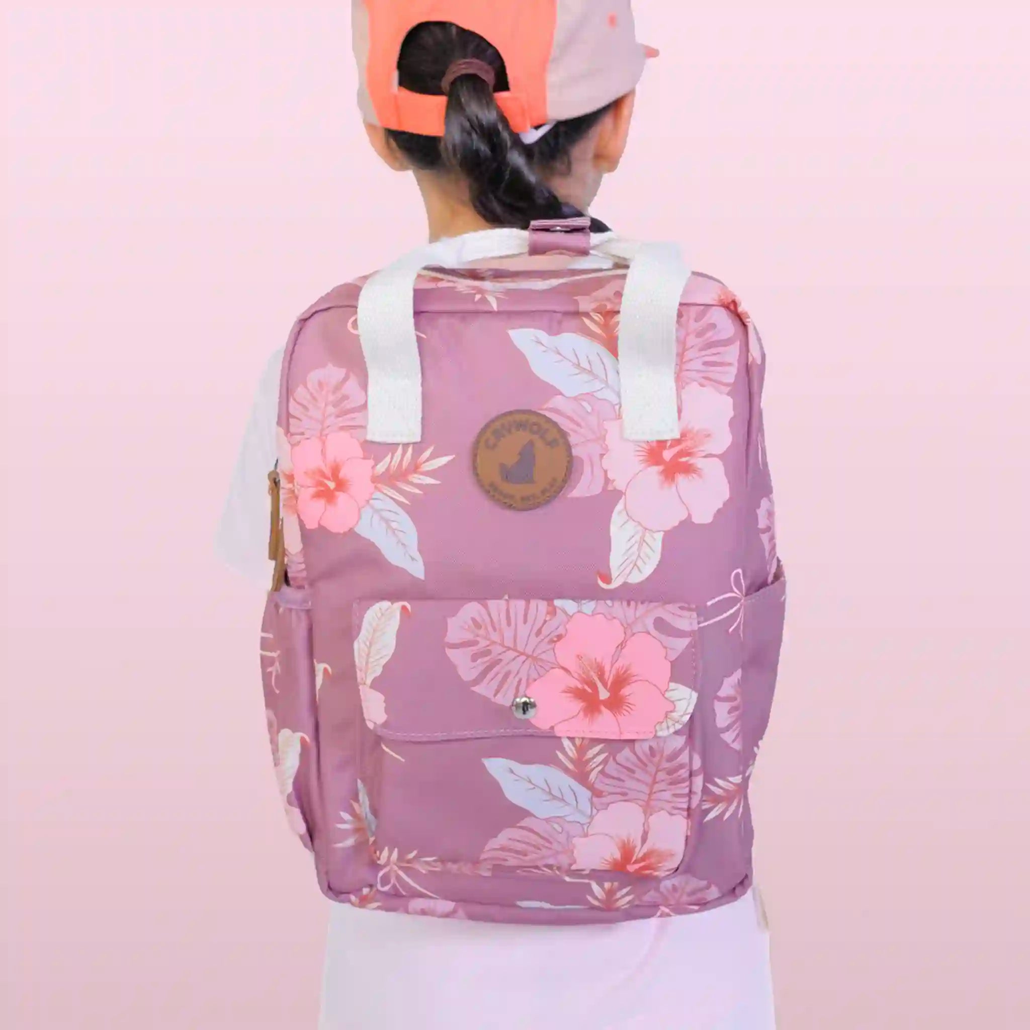 Person wearing a pink floral backpack against a light pink background