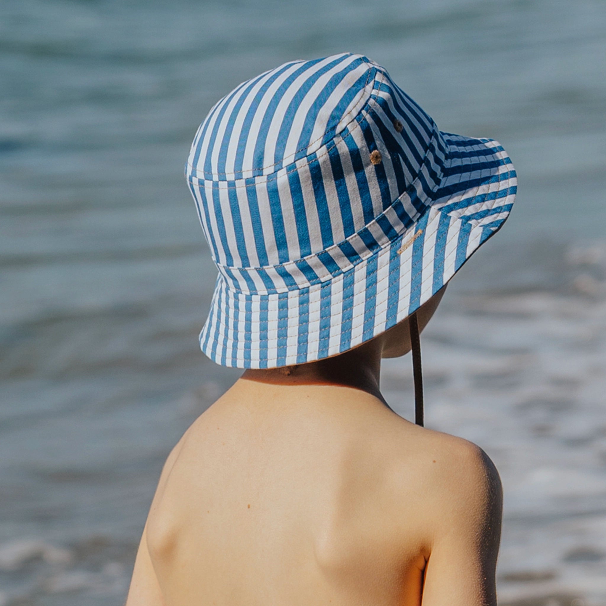 Person wearing a blue and white striped bucket hat by the water
