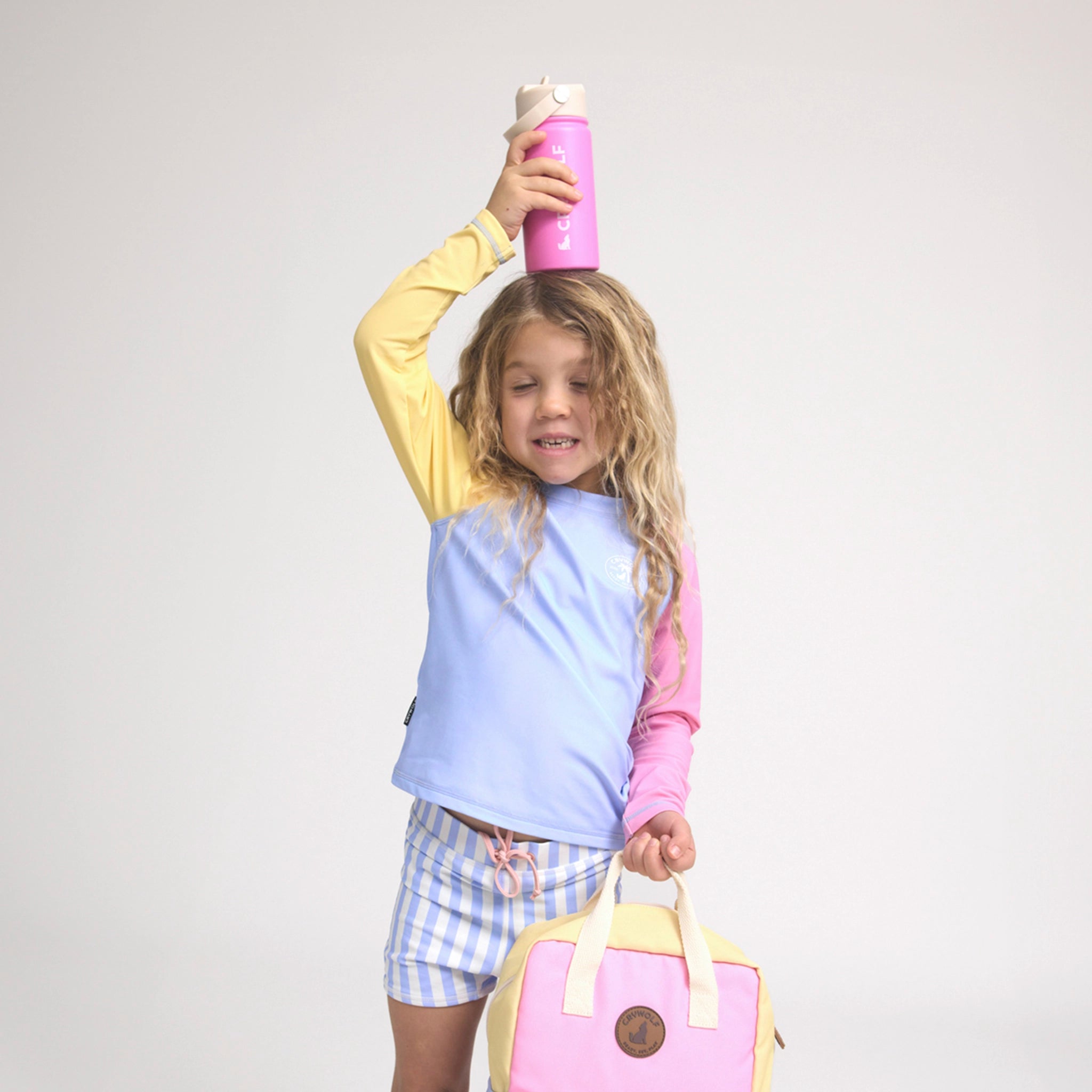 Child holding a pink water bottle and a yellow and pink backpack against a white background