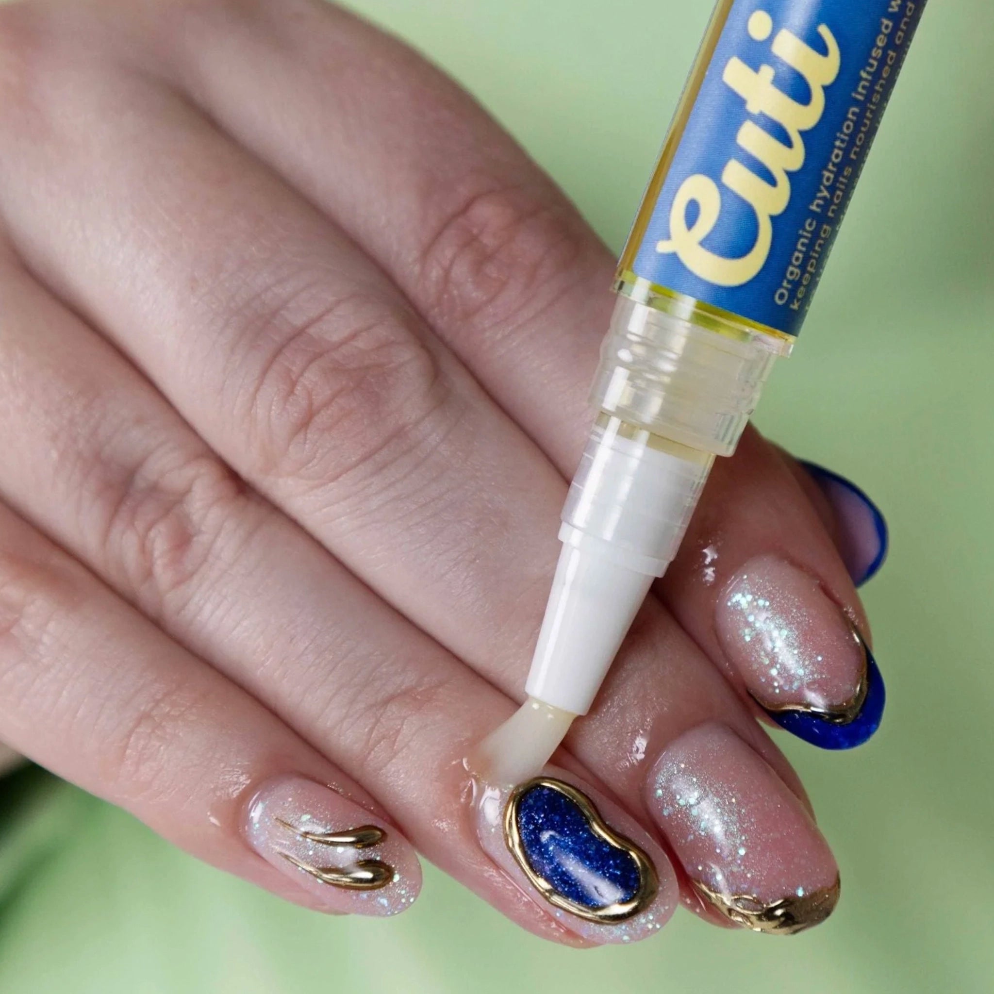 Hand applying a nail treatment with a 'Cuti' pen on a blurred green background