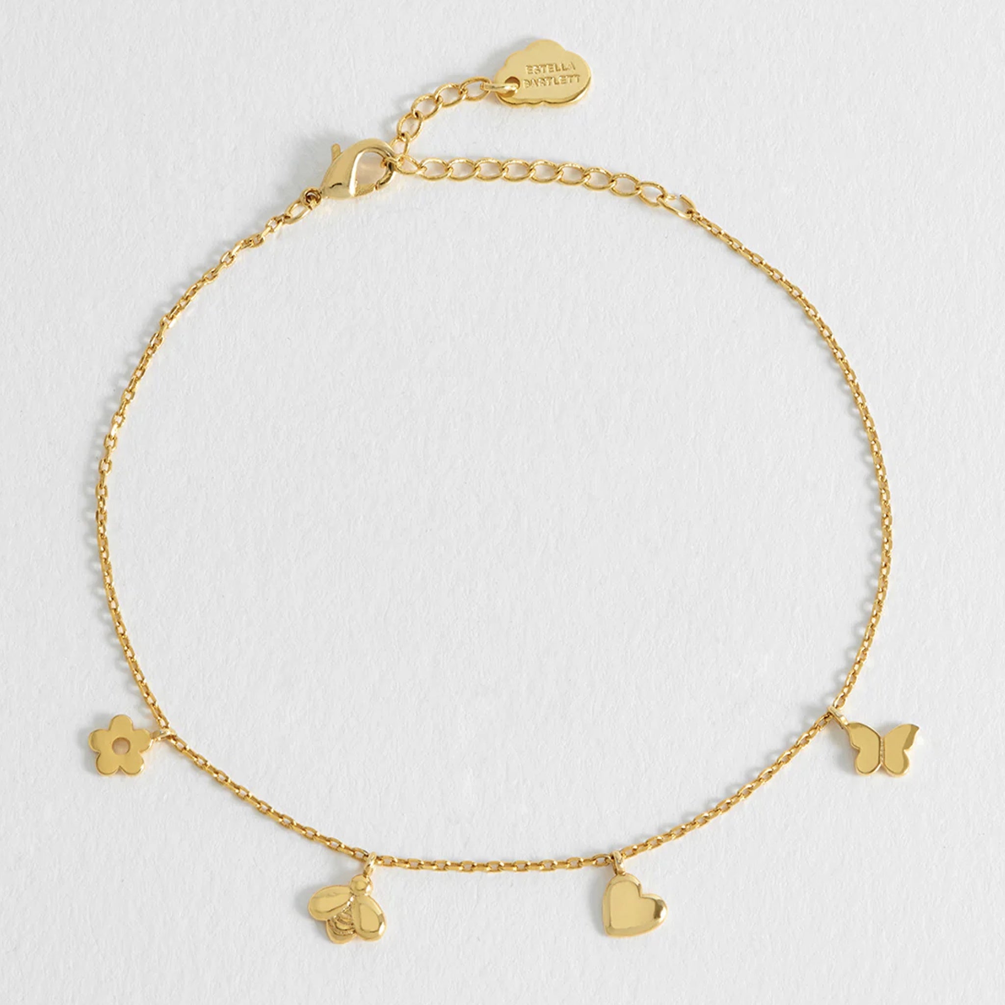 Gold bracelet with heart and flower charms on a light gray background