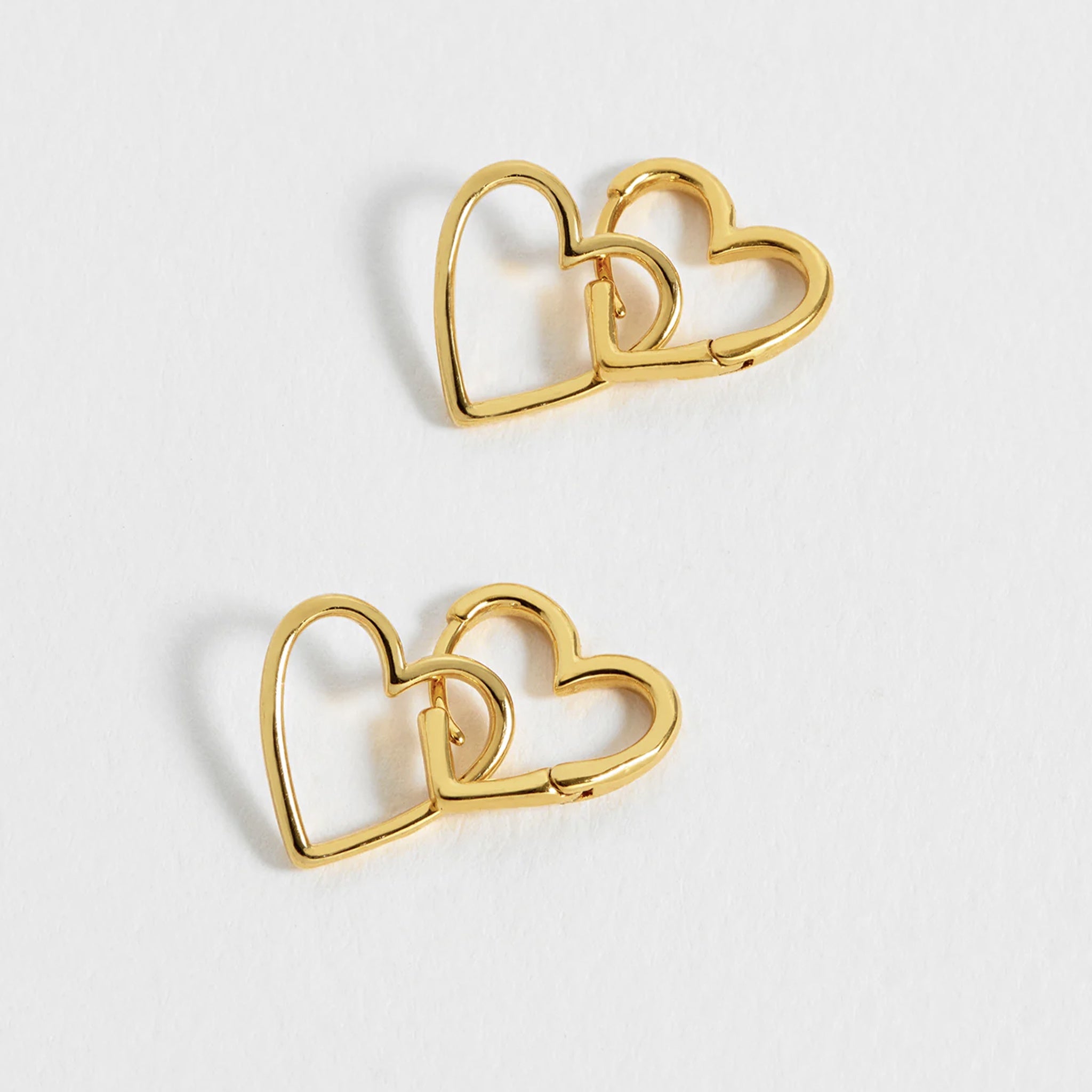 Gold heart-shaped earrings on a light gray background