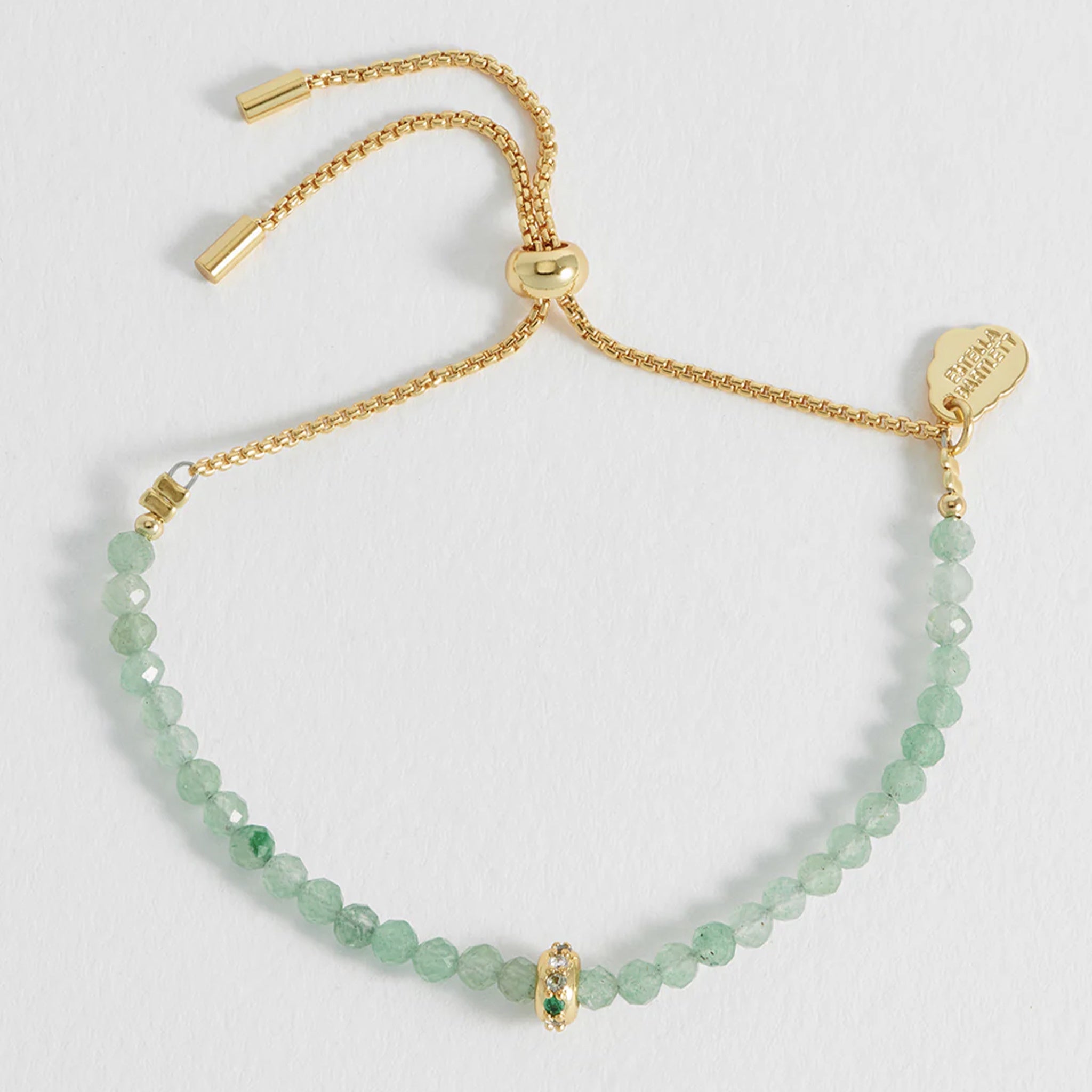 Gold bracelet with green beads on a light gray background