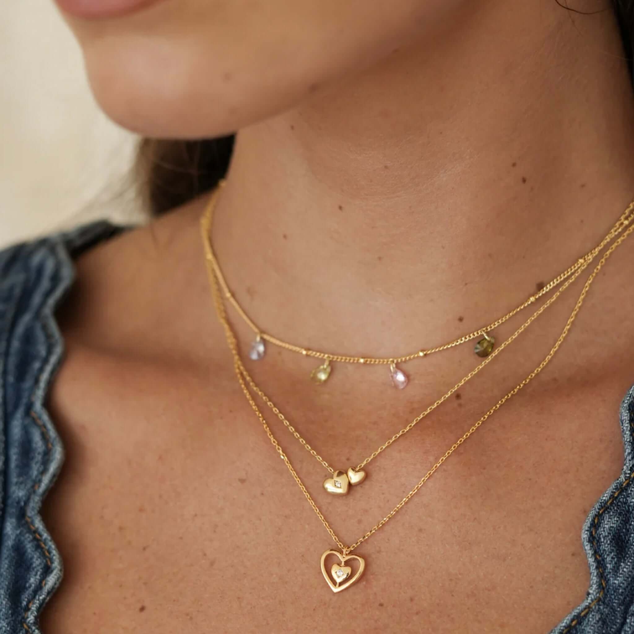 Alt Tag: Estella Bartlett Enveloped Heart CZ Necklace - Gold Plated layered heart pendant necklace on model, sparkling cubic zirconia