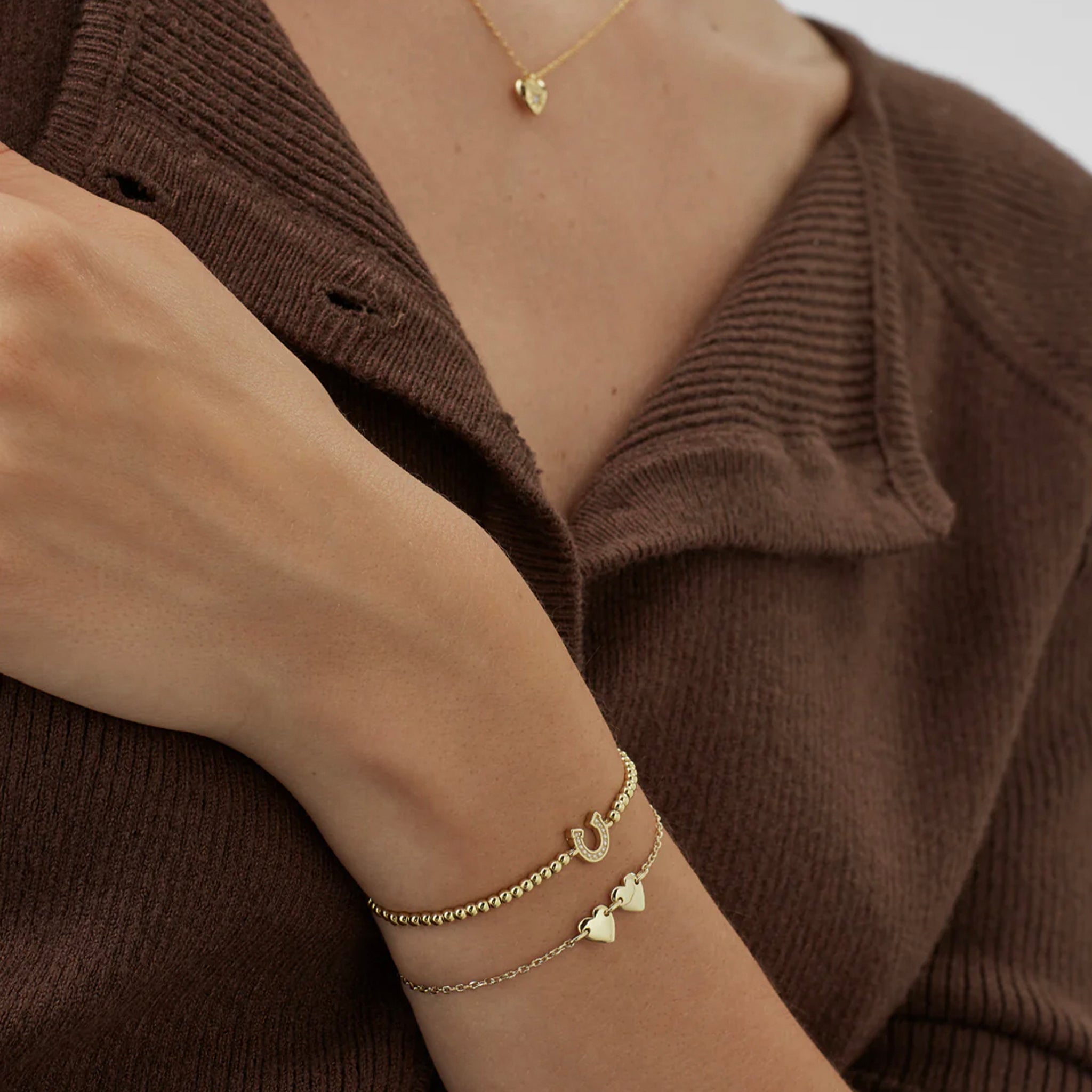 Close-up of a person wearing a brown sweater with gold jewelry on a neutral background