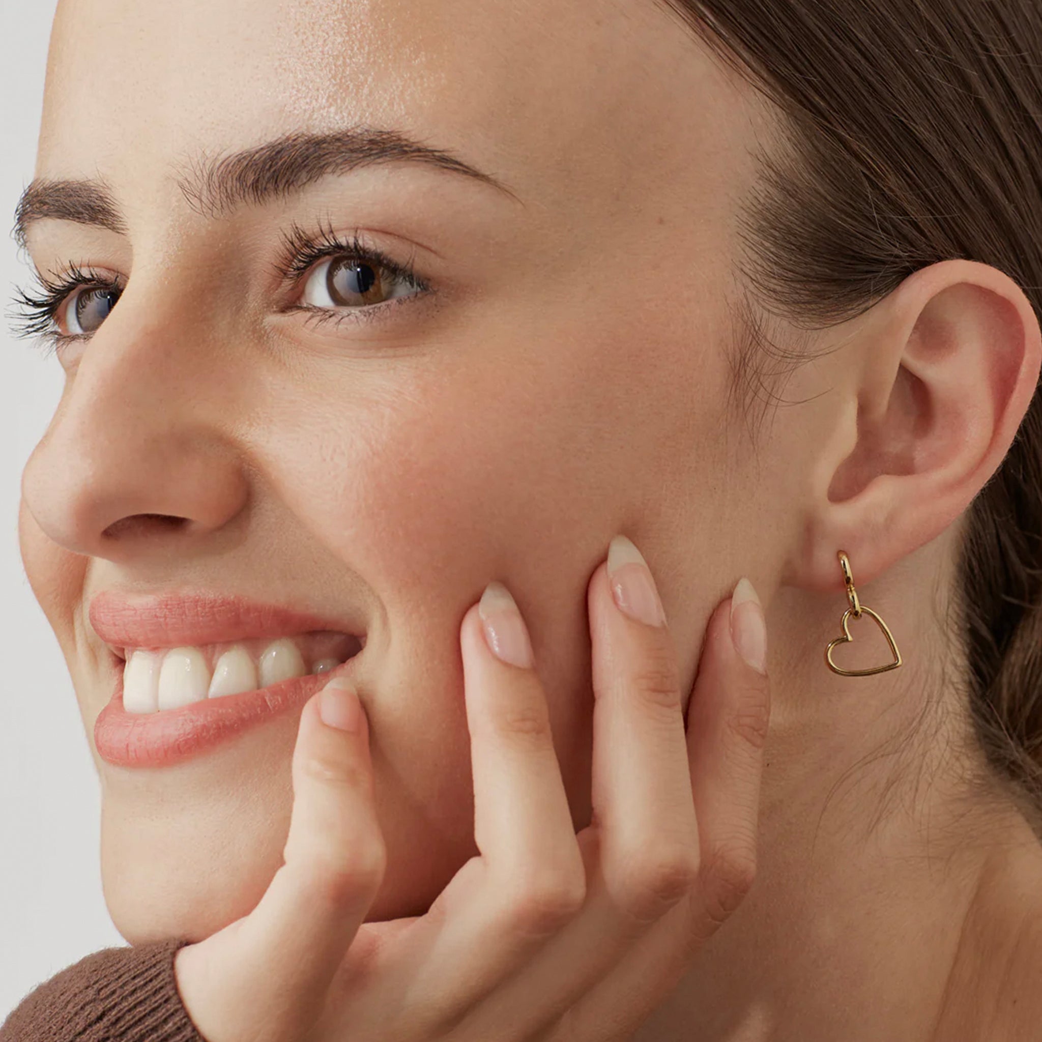 Close-up of a woman wearing a gold heart-shaped earring with a plain background