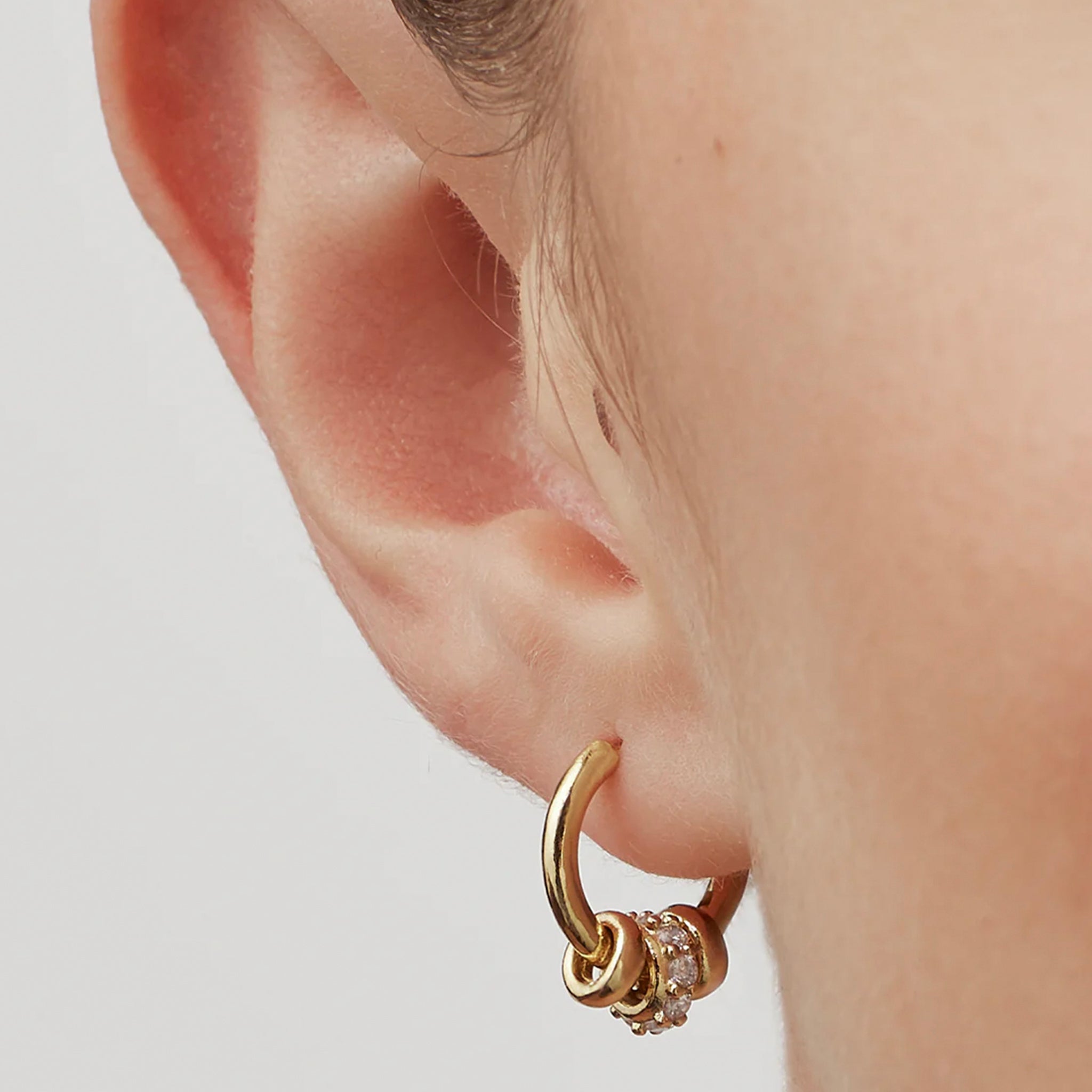 Gold hoop earring with small diamonds worn by a person on a light background