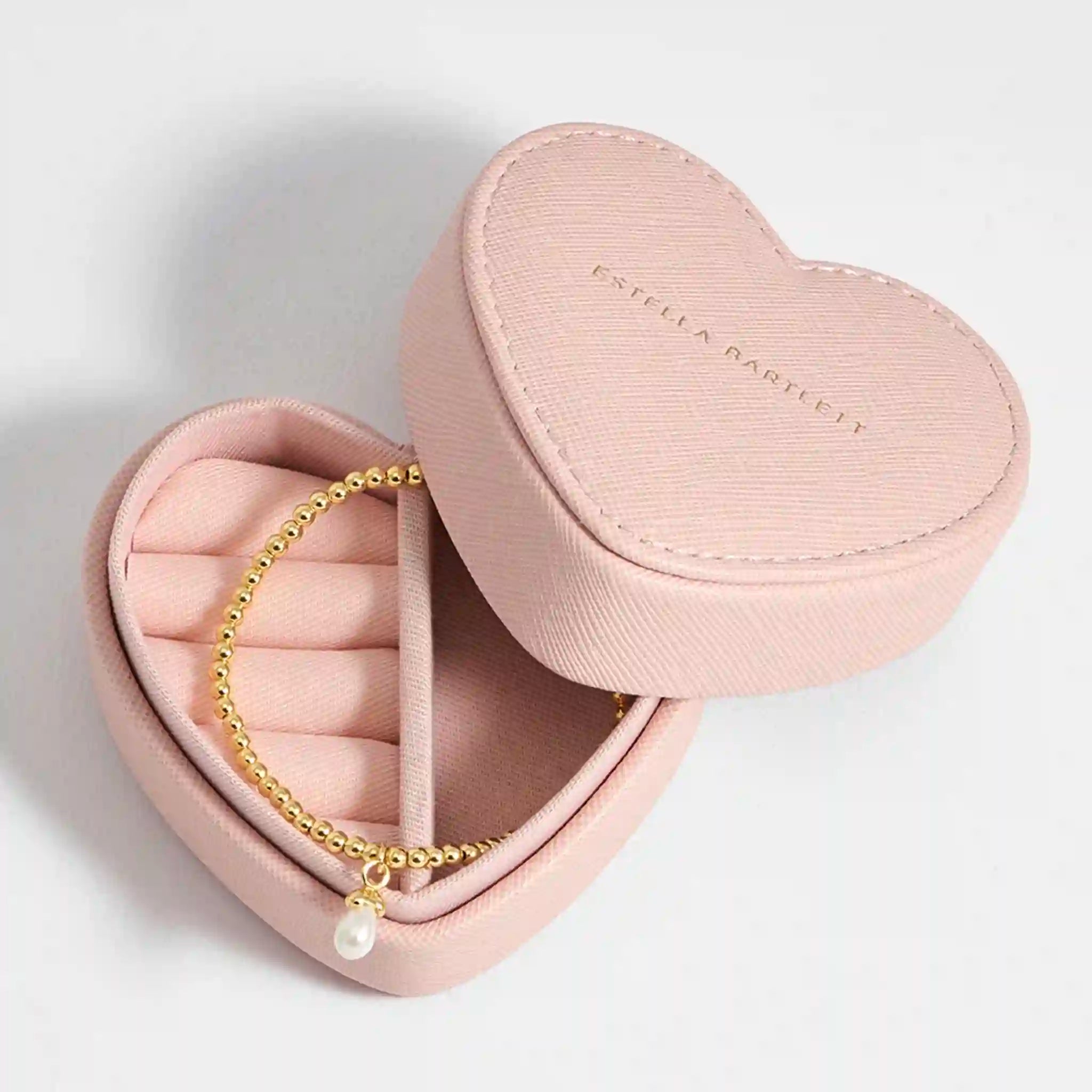 Heart-shaped pink jewelry box with a gold bracelet featuring a pearl charm on a light gray background.