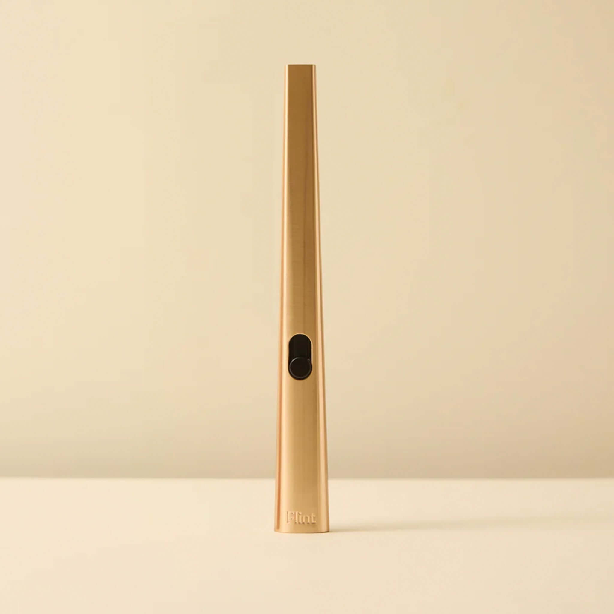 Gold cylindrical lighter with a black button on a beige background