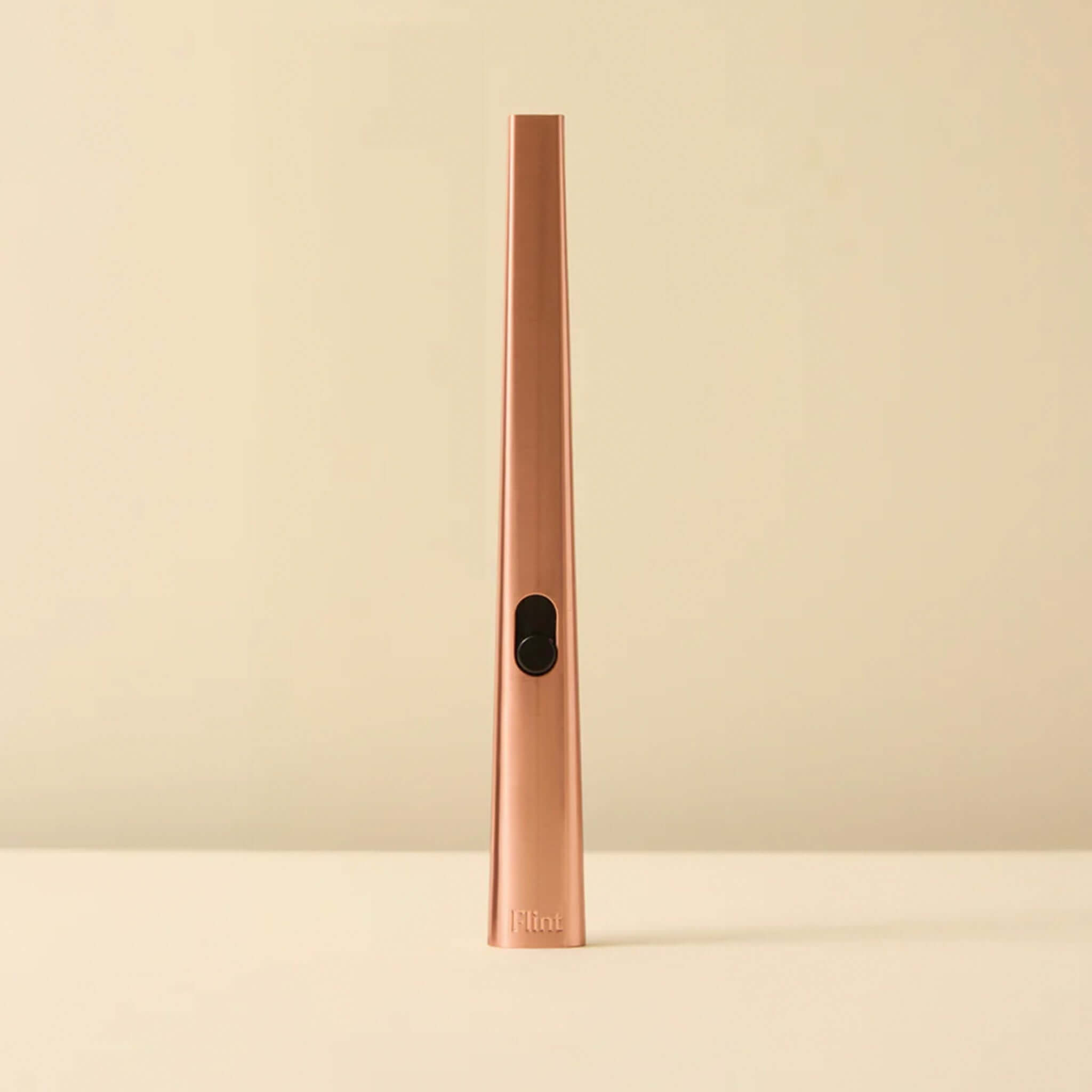 Rose gold lighter with black button on a beige background