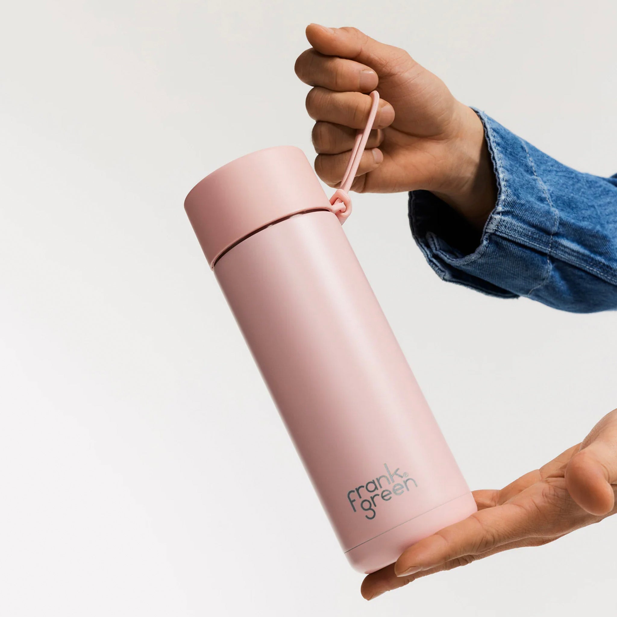 Hand holding a pink reusable water bottle with Frank Green logo on a neutral background