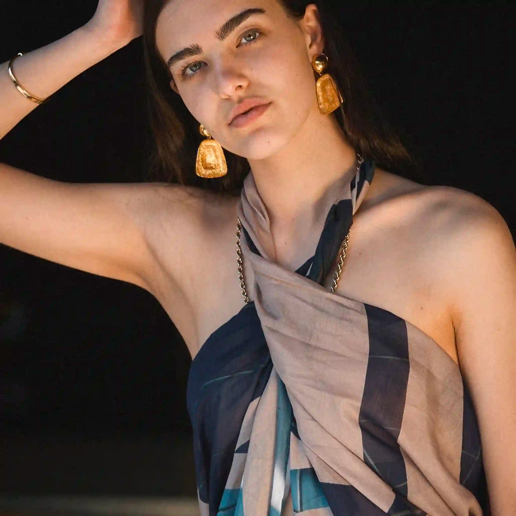 Woman wearing a patterned scarf and gold earrings against a dark background