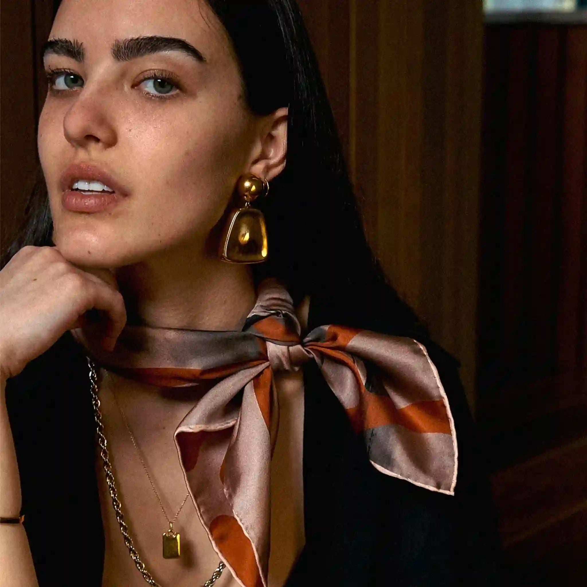 Woman wearing a patterned scarf and gold earrings with a blurred background