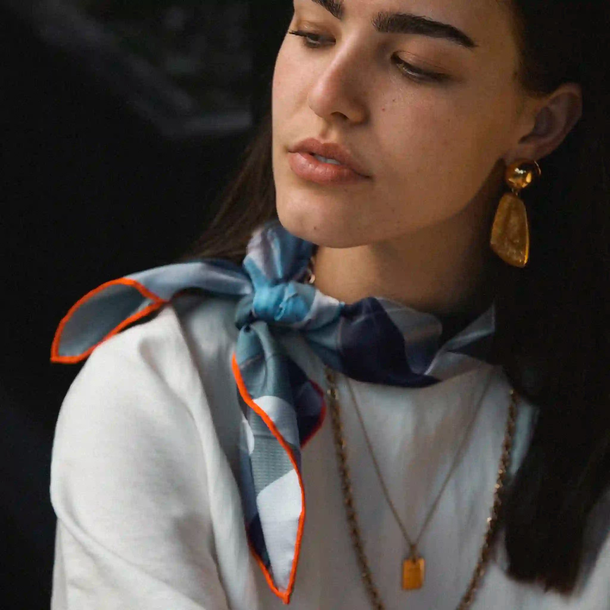 Woman wearing a patterned scarf and gold earrings with a dark background