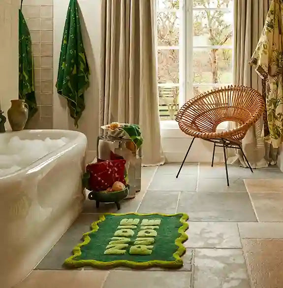 Bathroom with a green bath mat on the floor, bathtub, and window.