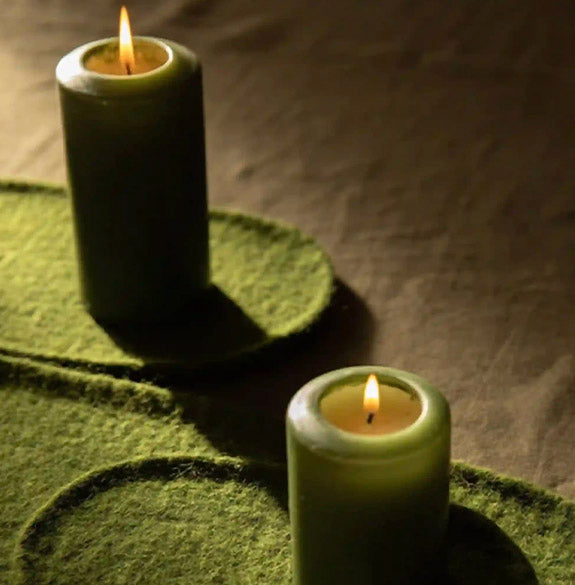 Two green candles on a textured surface with a blurred background