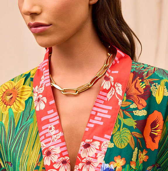 Woman wearing a colorful floral kimono with a gold necklace against a beige background
