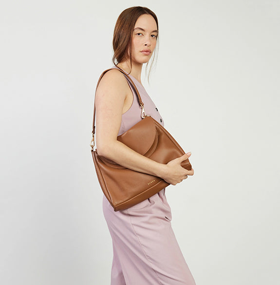 Woman holding a brown leather handbag against a plain background