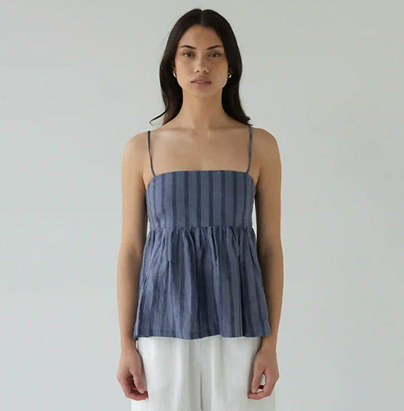 Woman wearing a blue striped top and white pants against a plain background