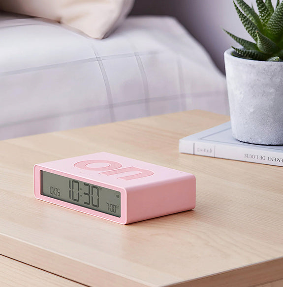 Pink digital clock on a wooden surface with a blurred background